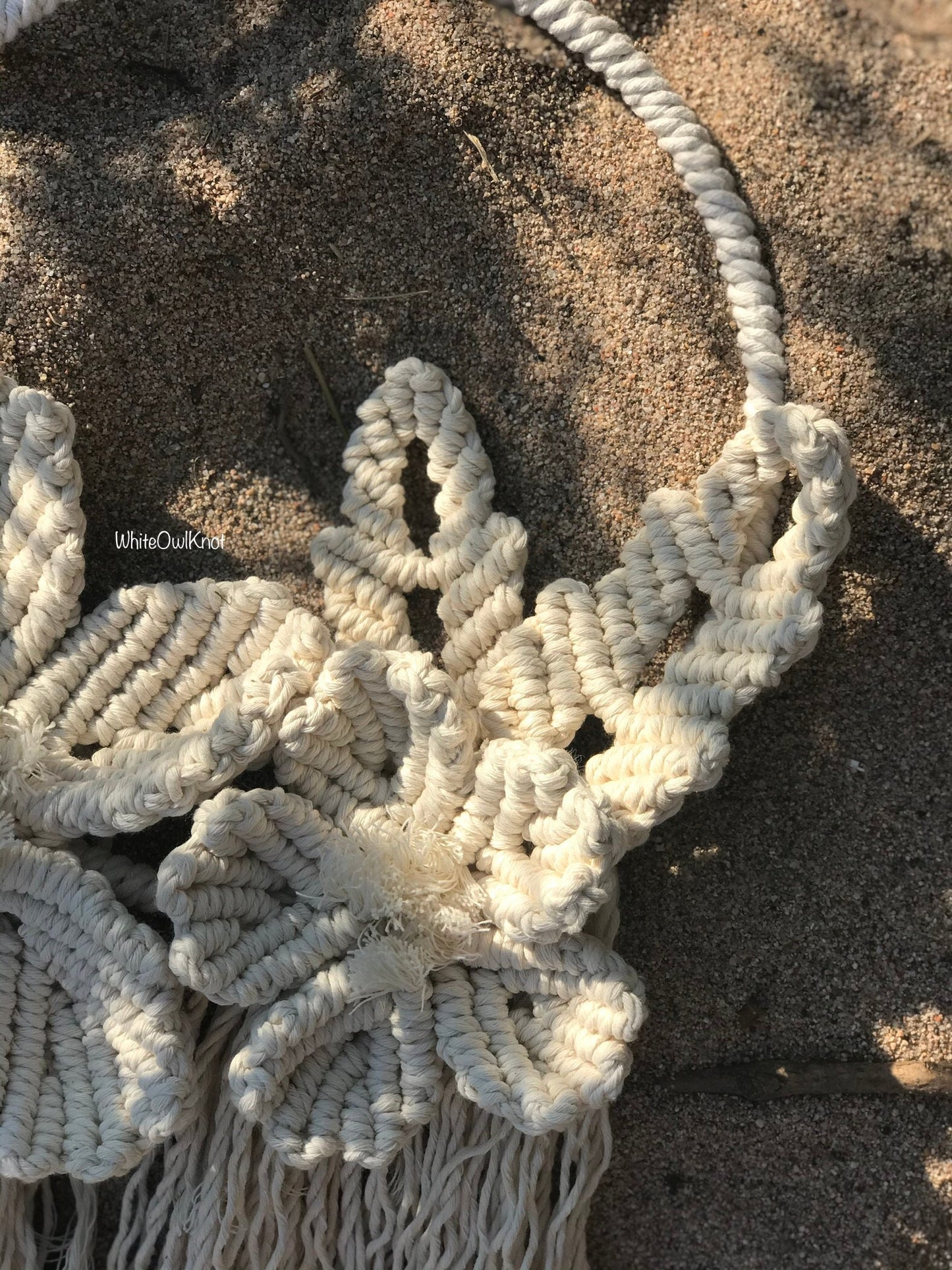 Close-up of a macrame wall hanging on sandy ground
