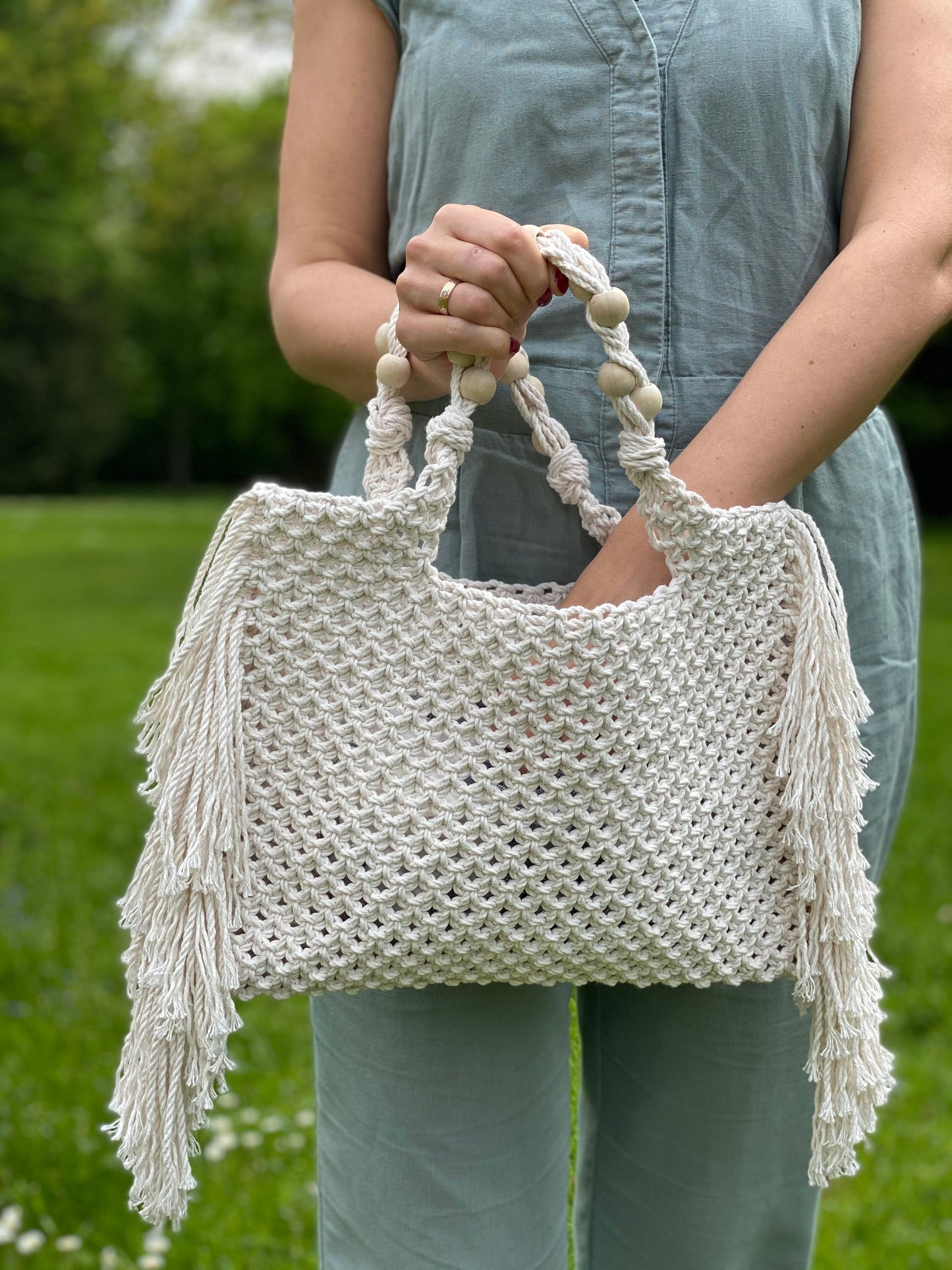 Person holding a white woven handbag with fringe details outdoors.