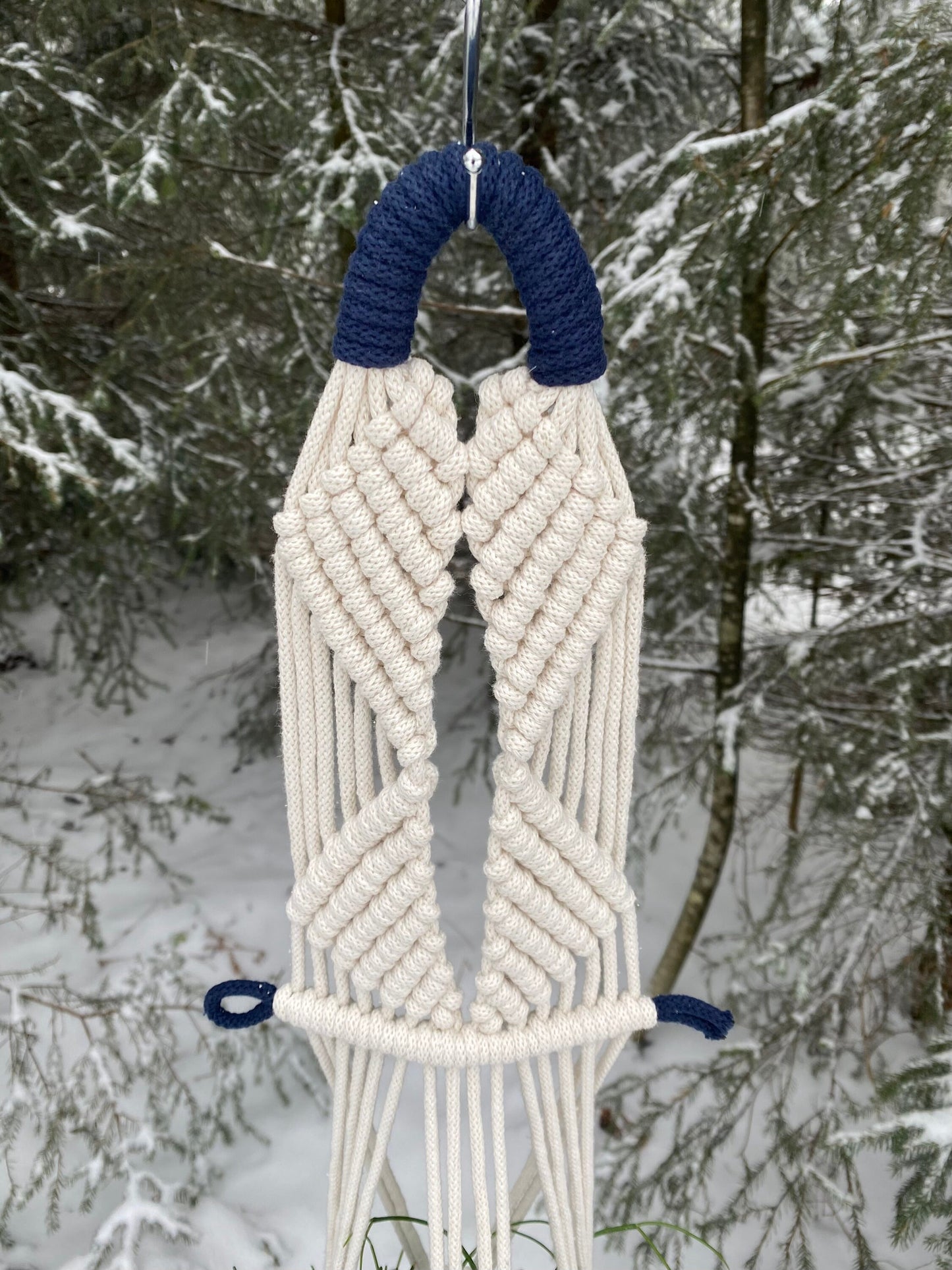 Macrame wall hanging with blue accents against a snowy forest background