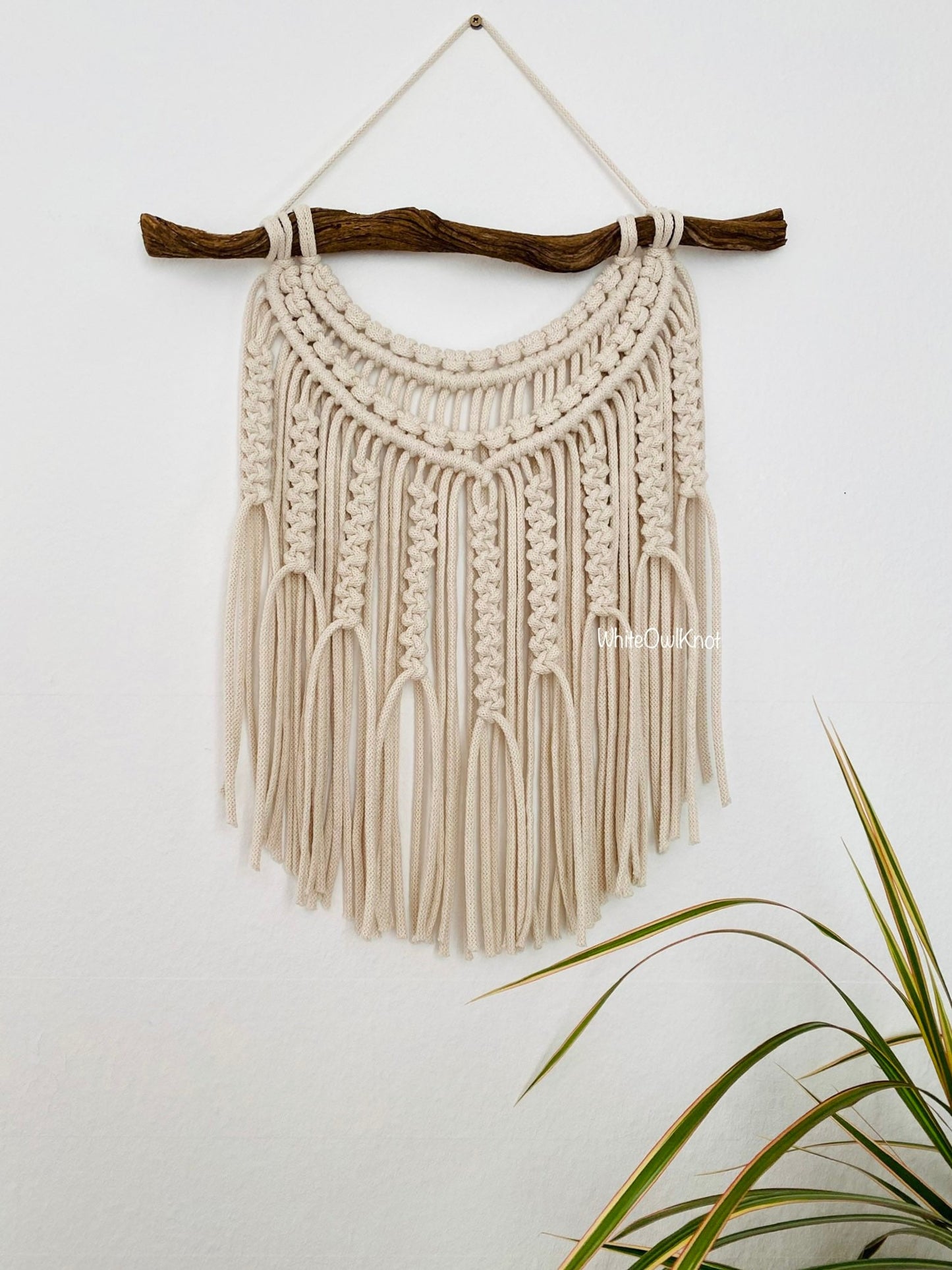Macrame wall hanging with natural materials on a plain background
