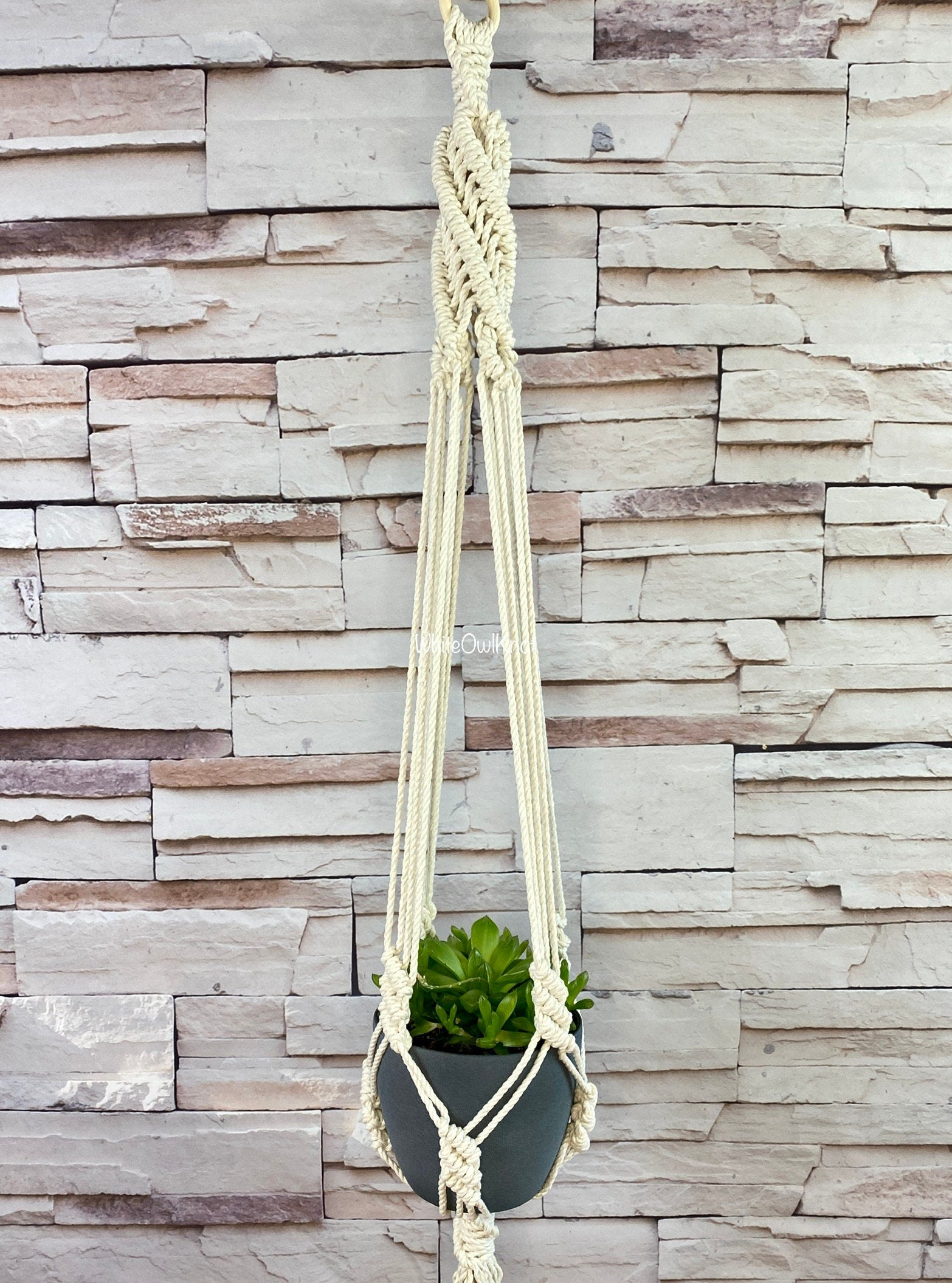 Macrame plant hanger with a plant against a stone wall background