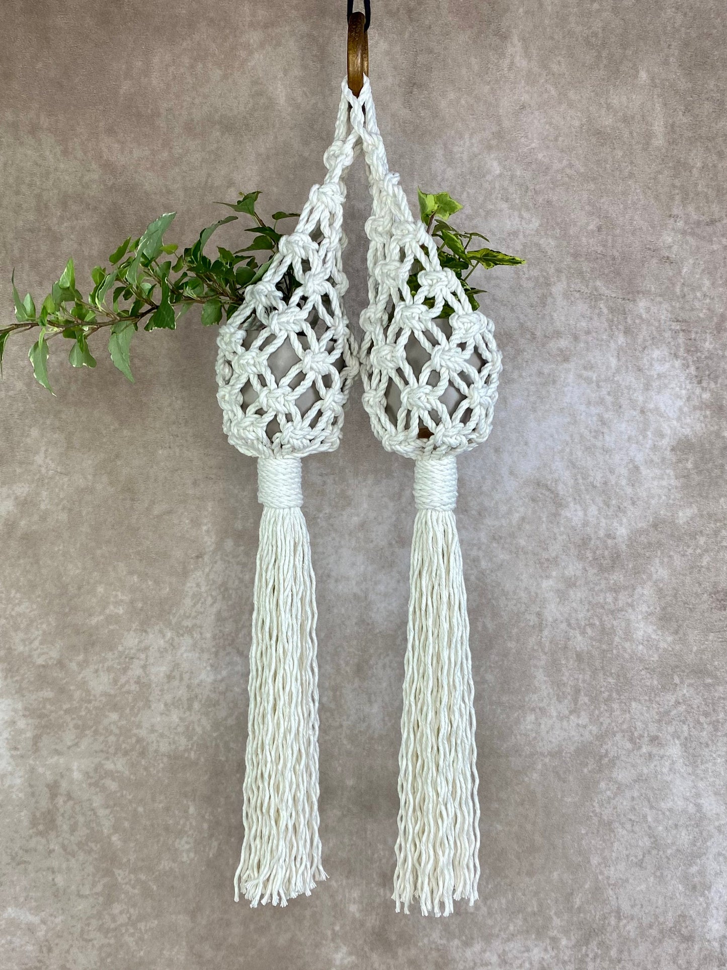 Two white macrame plant hangers with tassels on a gray background