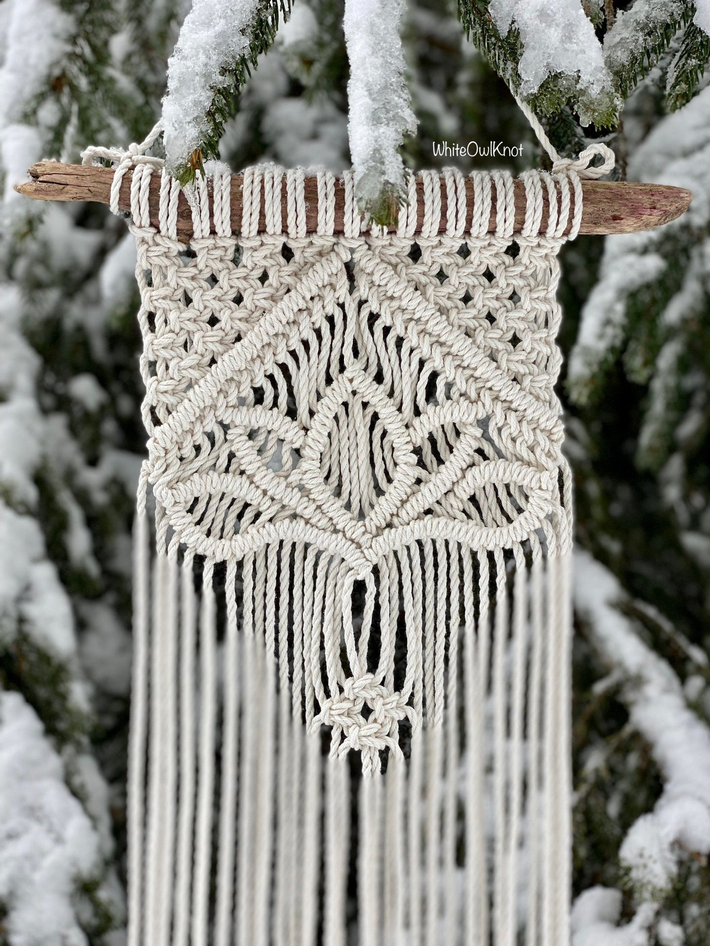 Macrame wall hanging with intricate patterns against a snowy tree background