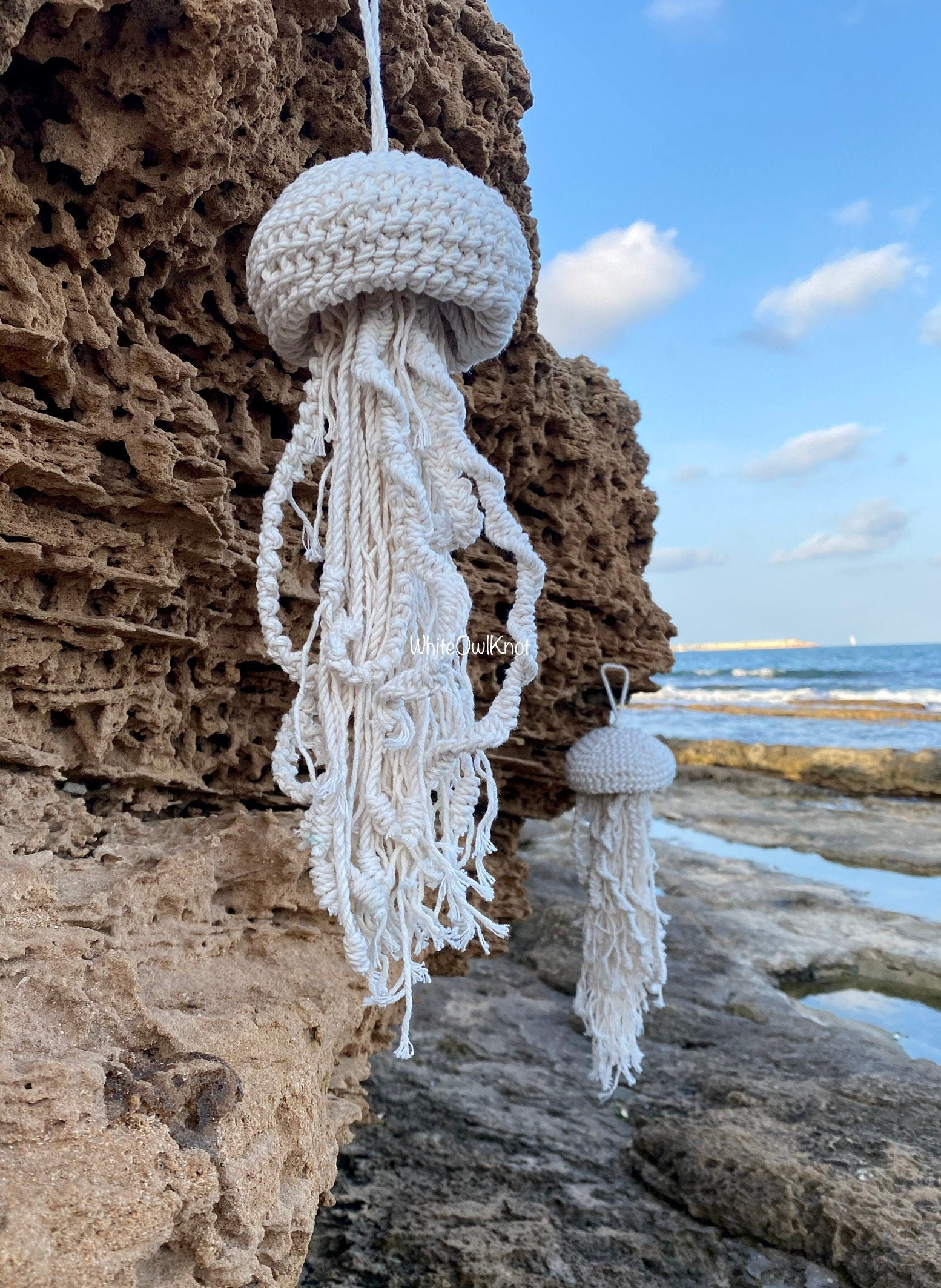 White jellyfish-shaped decorative item on a rocky beach with ocean and sky in the background