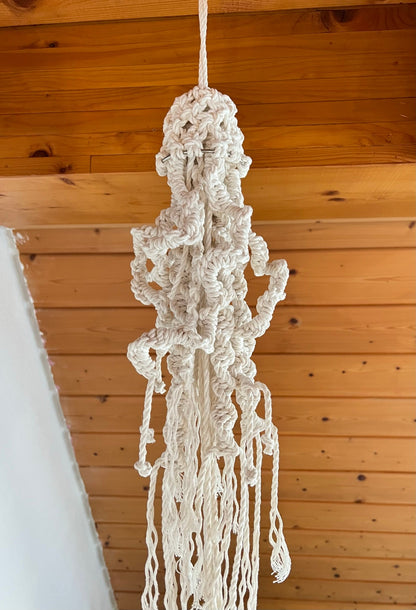 Macrame jellyfish hanger hanging against a wooden ceiling.