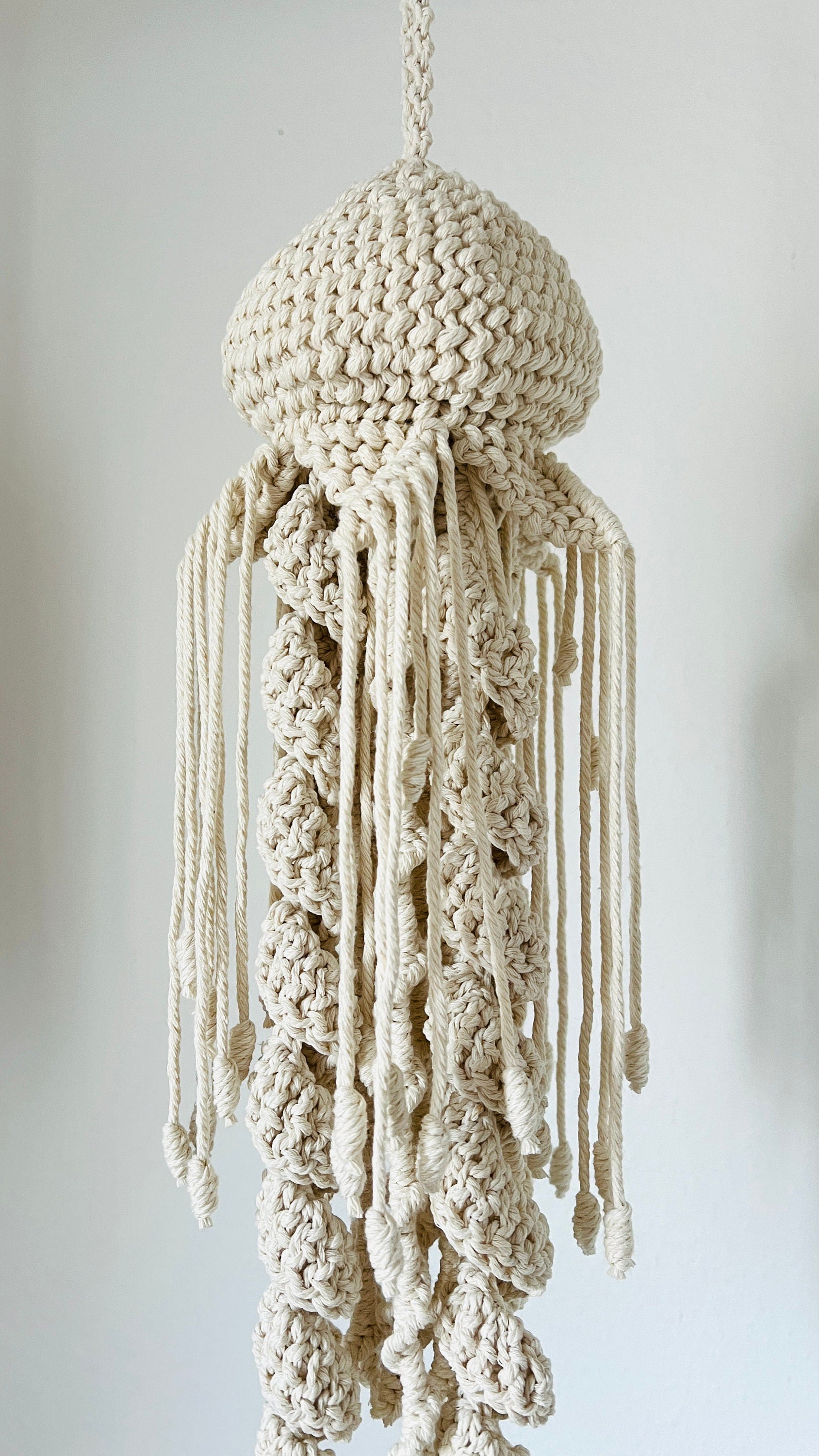 Macrame jellyfish mobile hanging against a plain background