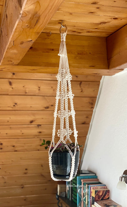 Macrame plant hanger with a pot of plants against a wooden wall.