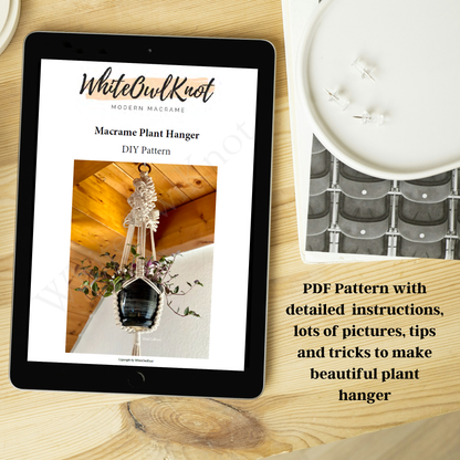 Tablet displaying a Macrame Plant Hanger DIY pattern on a wooden surface with a candle and plant in the background.