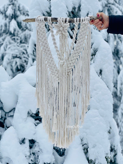 Macrame wall hanging held by a person against a snowy tree background
