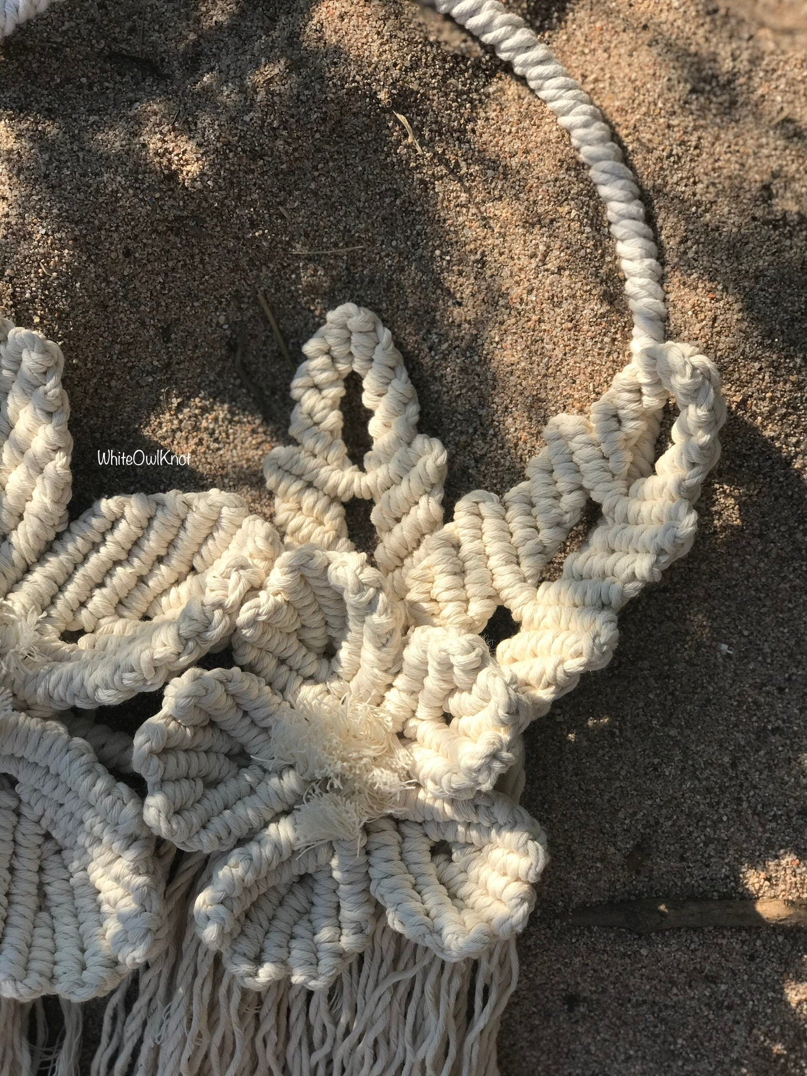 Close-up of a macrame wall hanging on sandy ground