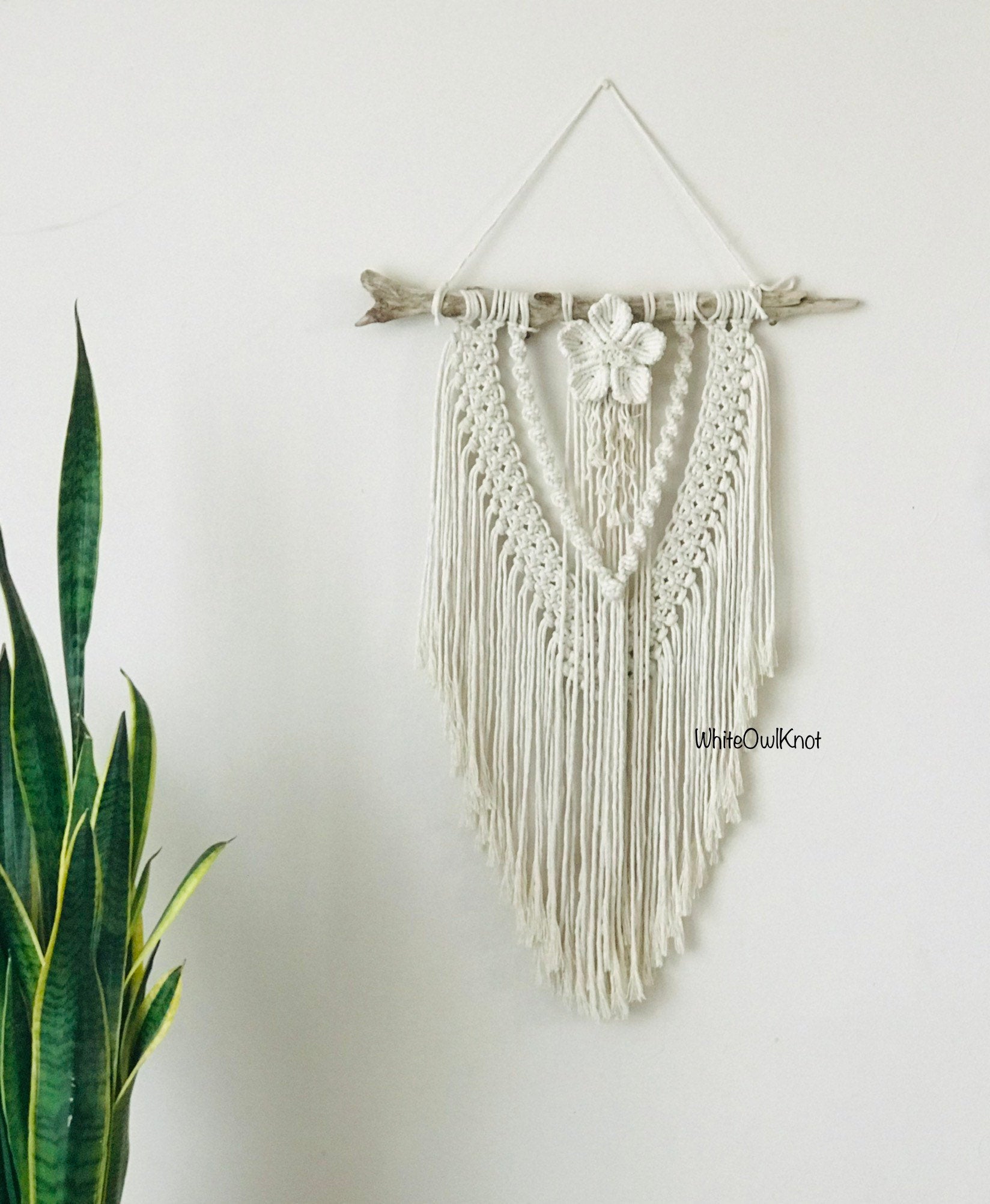 Macrame wall hanging with floral element on a white wall, featuring the brand 'White Owl Knot'.