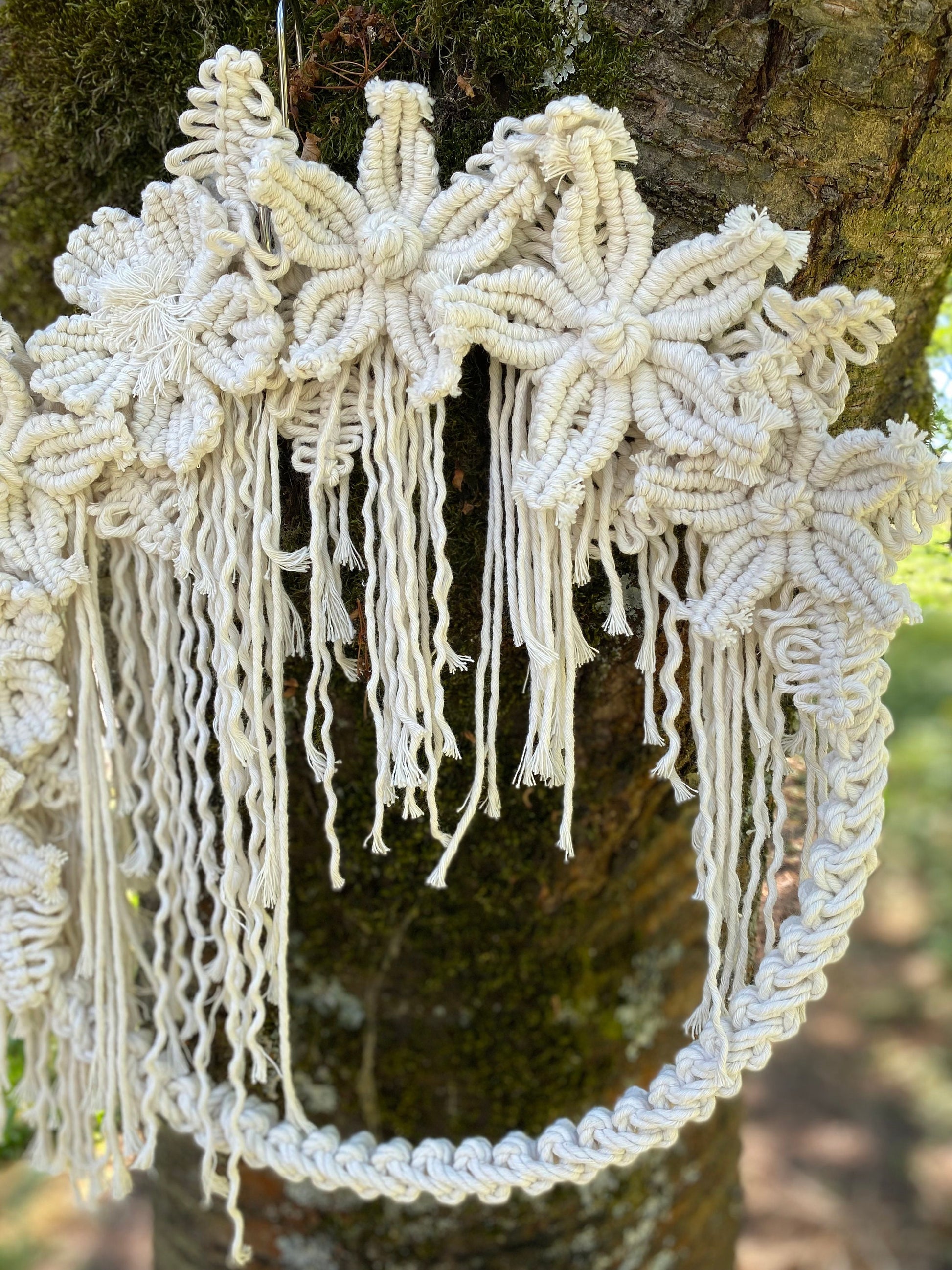 Decorative macrame wall hanging with floral patterns hanging on a tree.