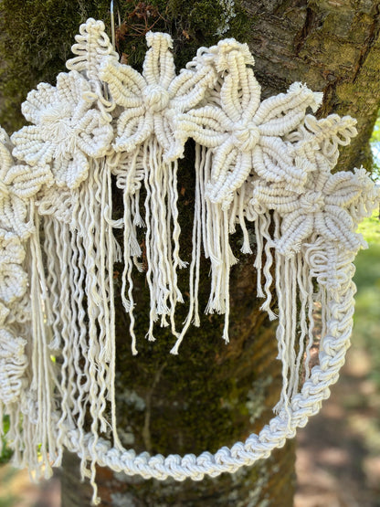 Decorative macrame wall hanging with floral patterns hanging on a tree.