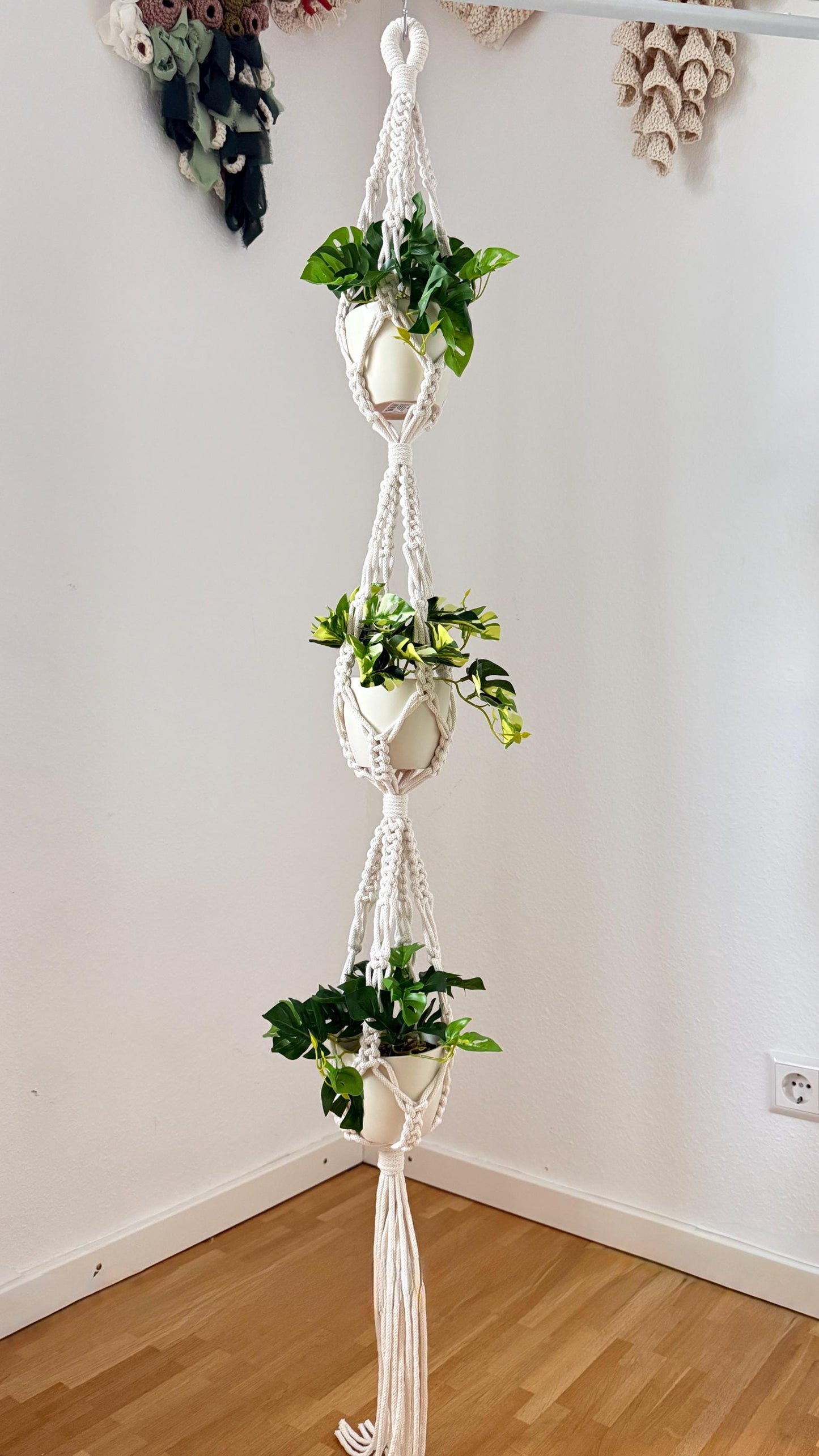 Macrame plant hanger with multiple plant pots against a white wall.