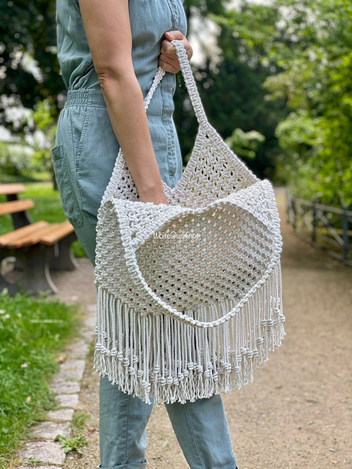 Woman holding a macrame bag outdoors with greenery in the background