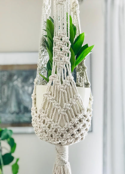 Macrame plant hanger with a plant against a neutral wall.
