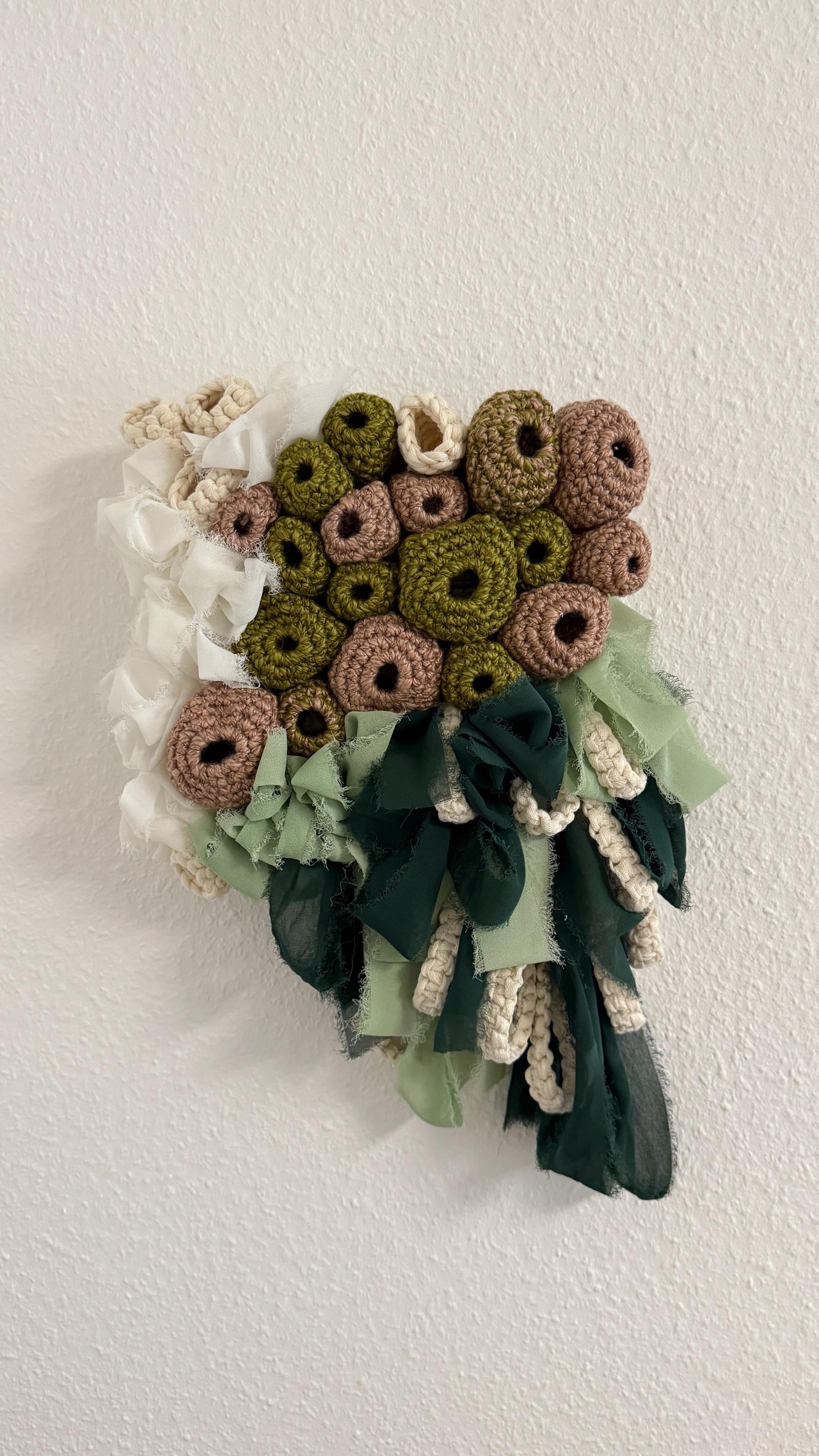 Crocheted flower wall art with green, brown, and white colors on a white background