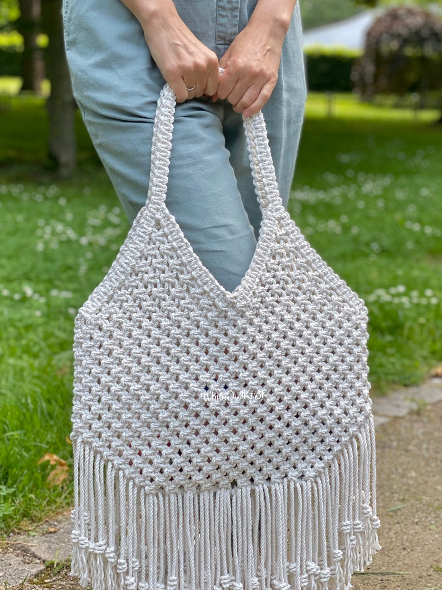 Person holding a woven bag with fringe in an outdoor setting