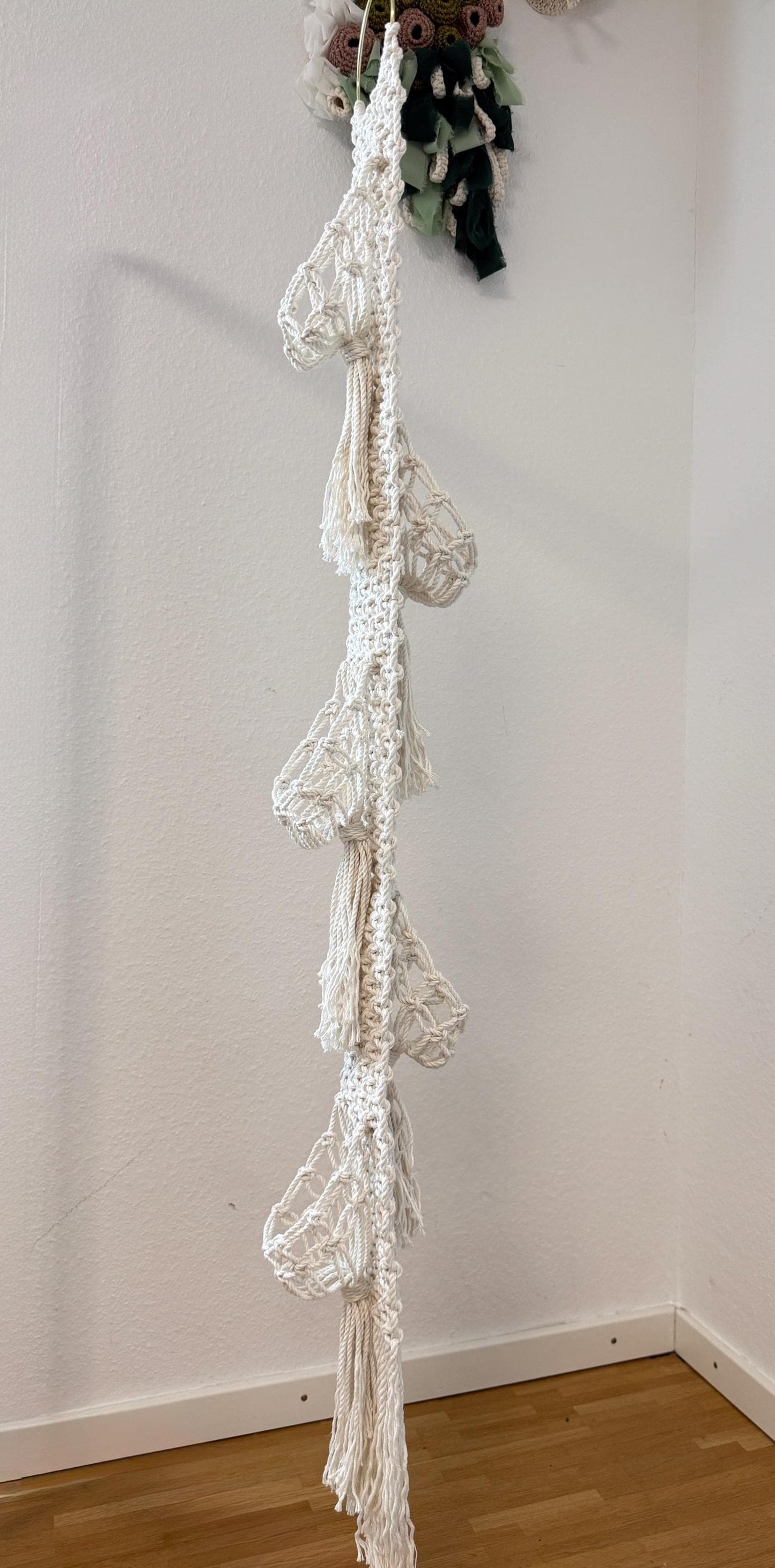 White macrame plant hanger hanging against a white wall.
