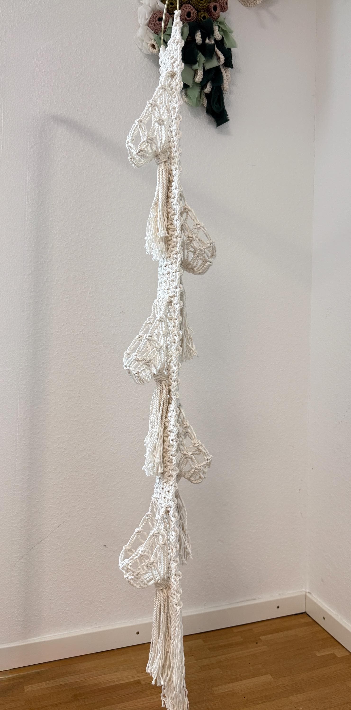 White macrame plant hanger hanging against a white wall.