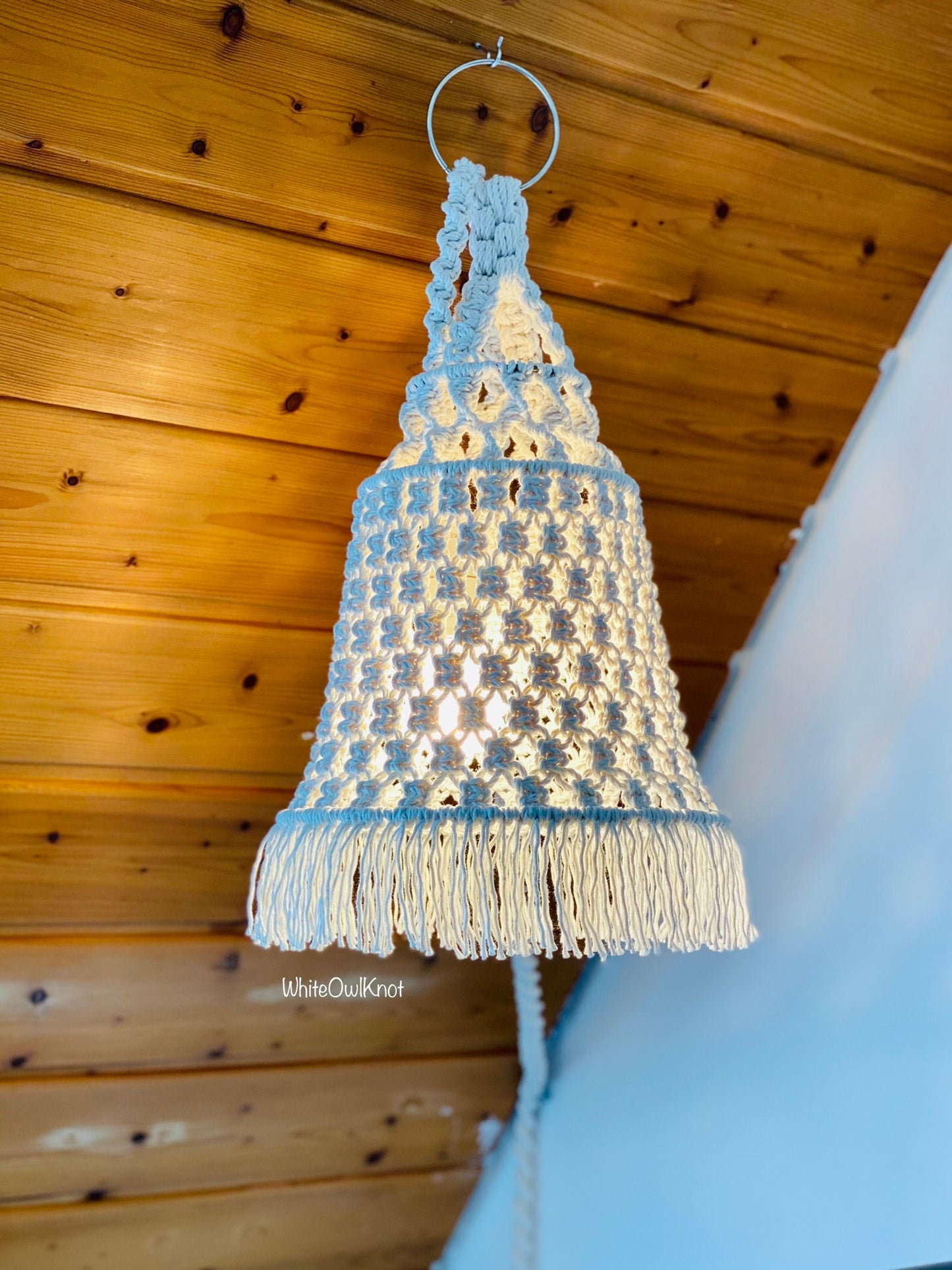 Macrame lampshade with tassels hanging against a wooden ceiling.
