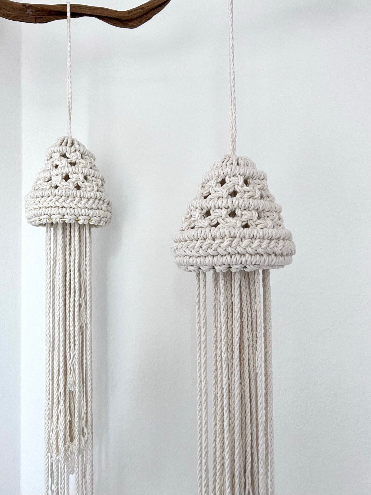 Two macrame jellyfish hanging against a white wall.