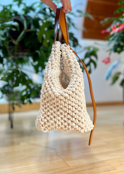 Beige woven handbag with brown leather handle held by a person indoors.
