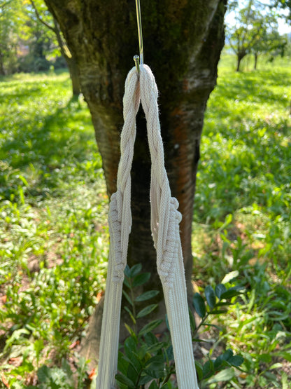 Macrame plant hanger hanging from a tree in a garden setting