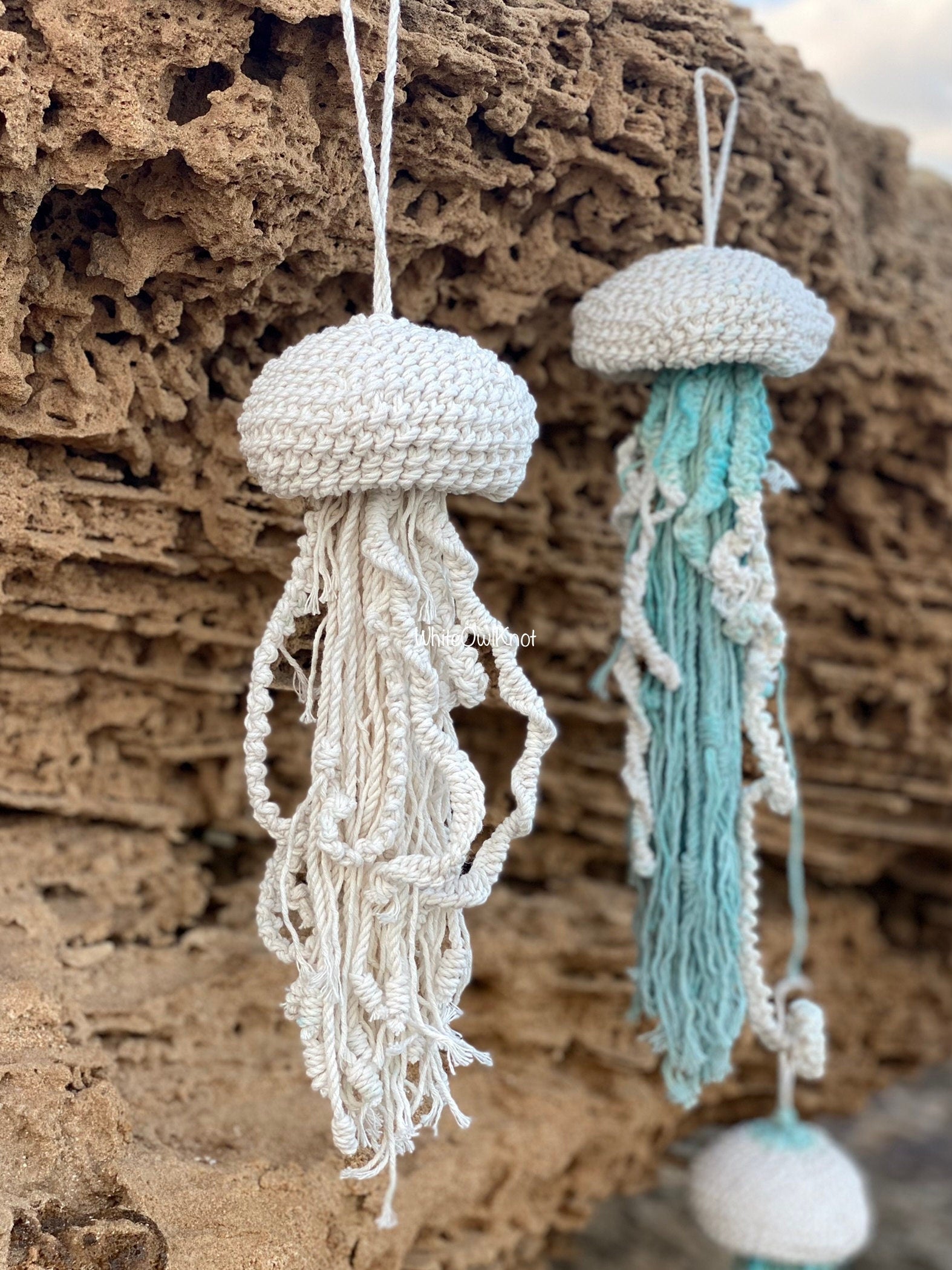 Two knitted jellyfish decorations hanging against a textured stone background.