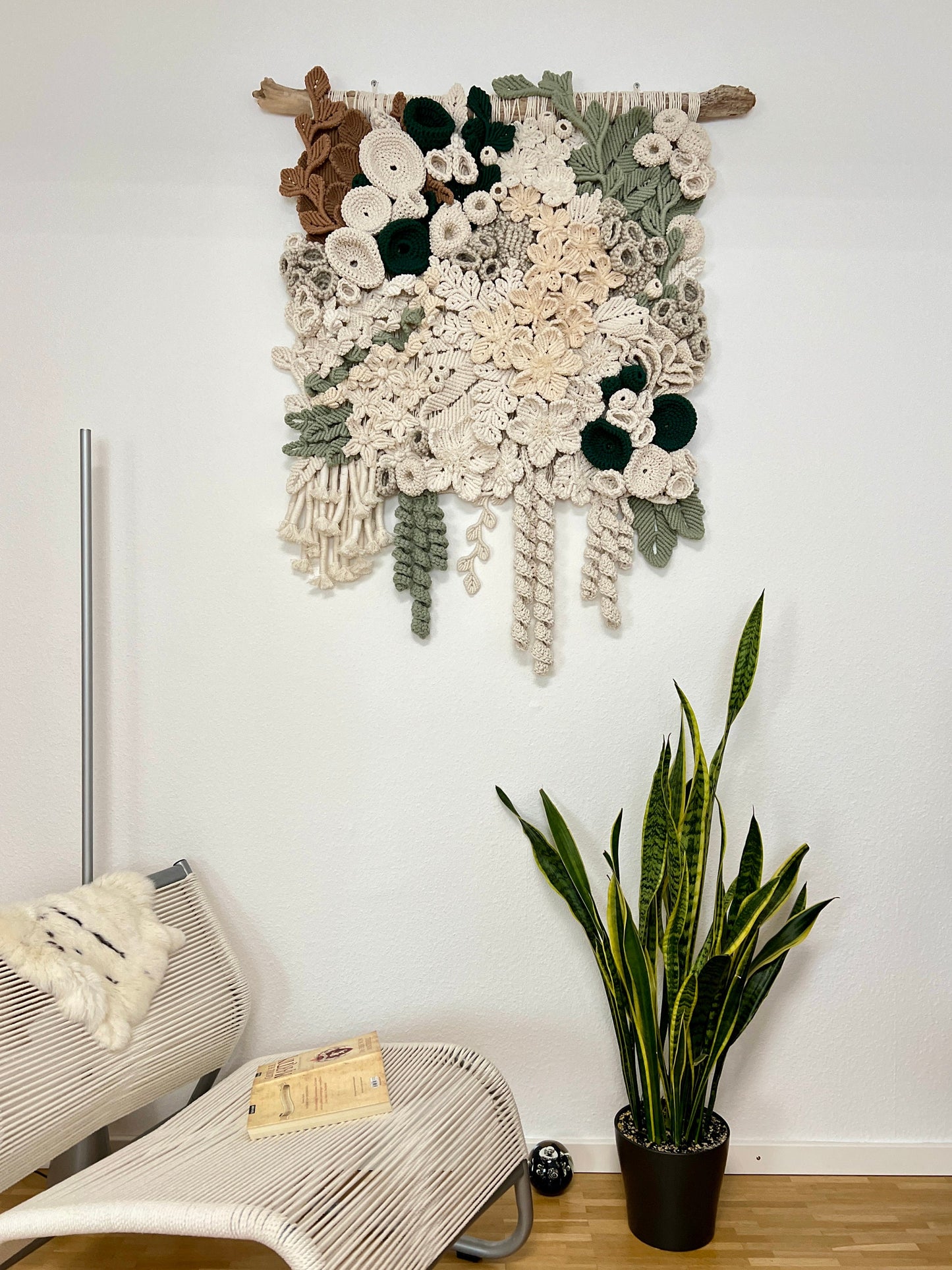 Decorative coral reef wall hanging with flowers and leaves above a chair and plant on a white wall.