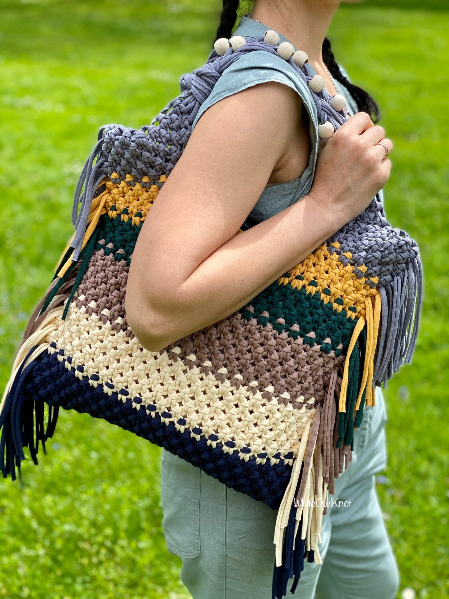 Person holding a colorful macrame bag with fringes against a green grass background