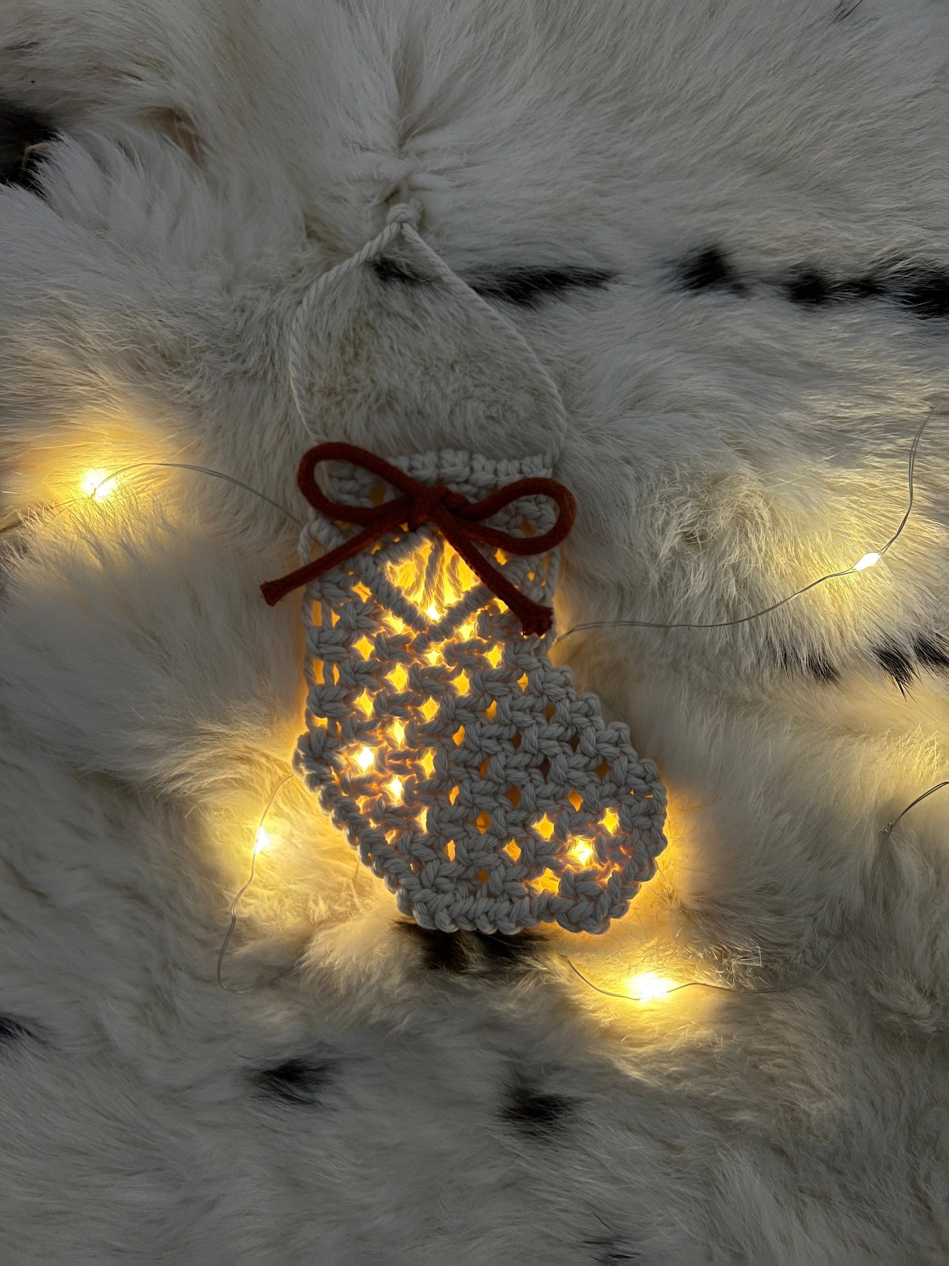 Decorative macrame Christmas Stocking with lights on a fluffy white surface