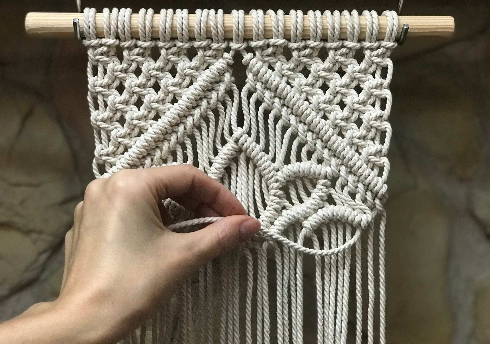 Handmade macrame wall hanging with a hand adjusting the strings against a neutral background