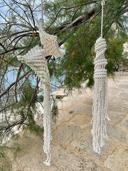 Macrame jellyfish decor hanging from a tree branch with a stone wall in the background.