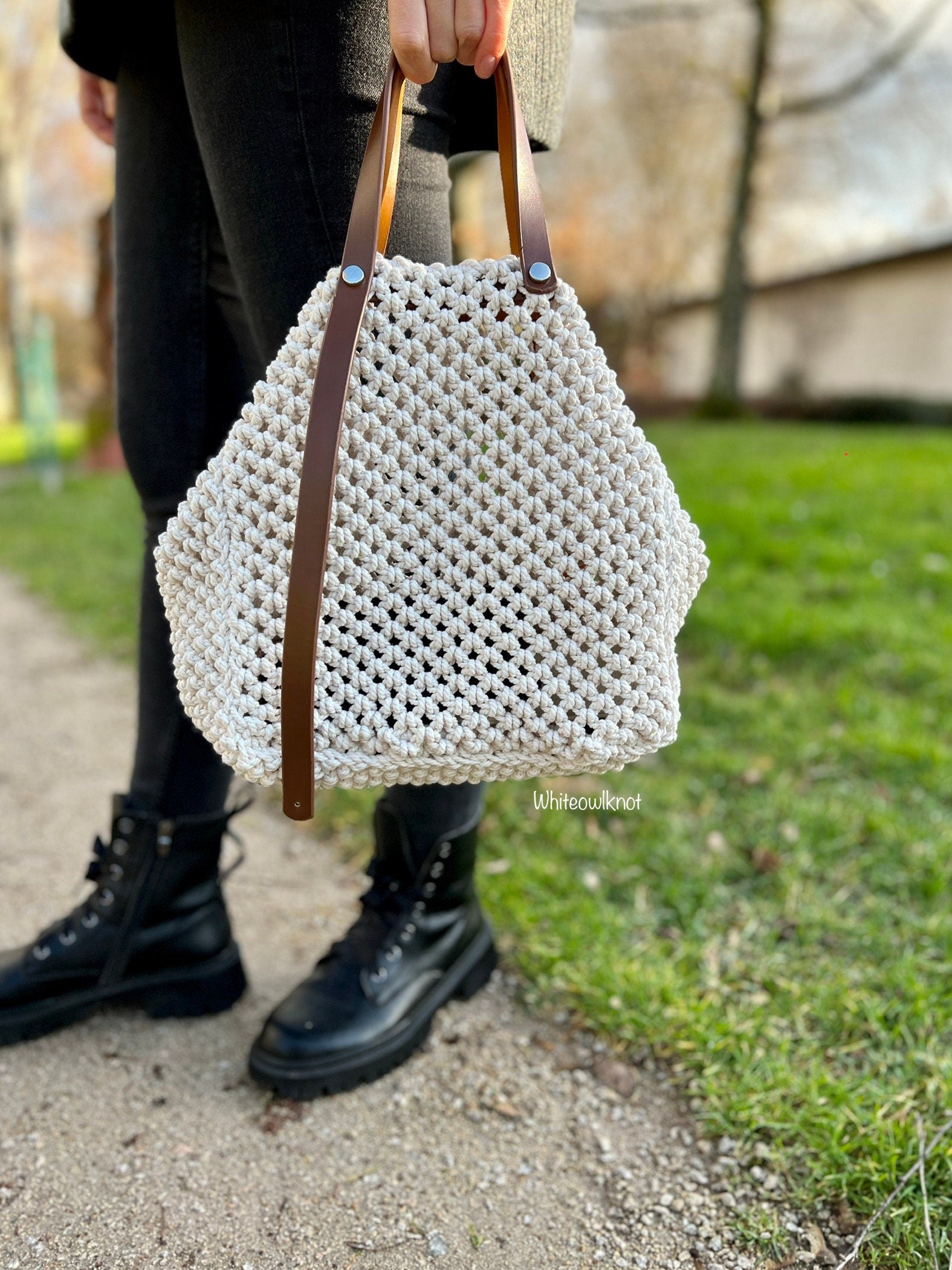 White woven handbag with brown handles held by a person on a path outdoors.