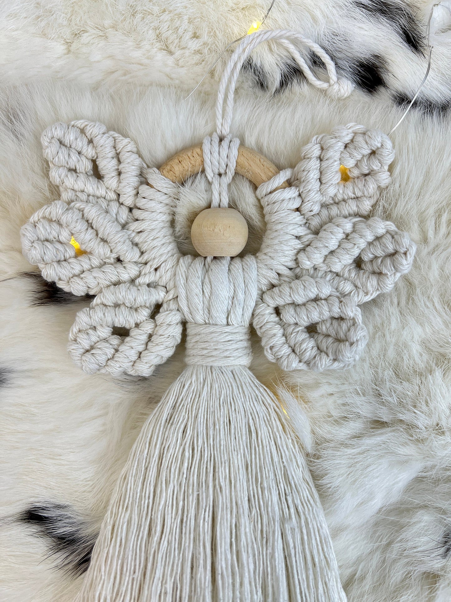 Macrame christmas angel ornament with wooden center on a fluffy white background