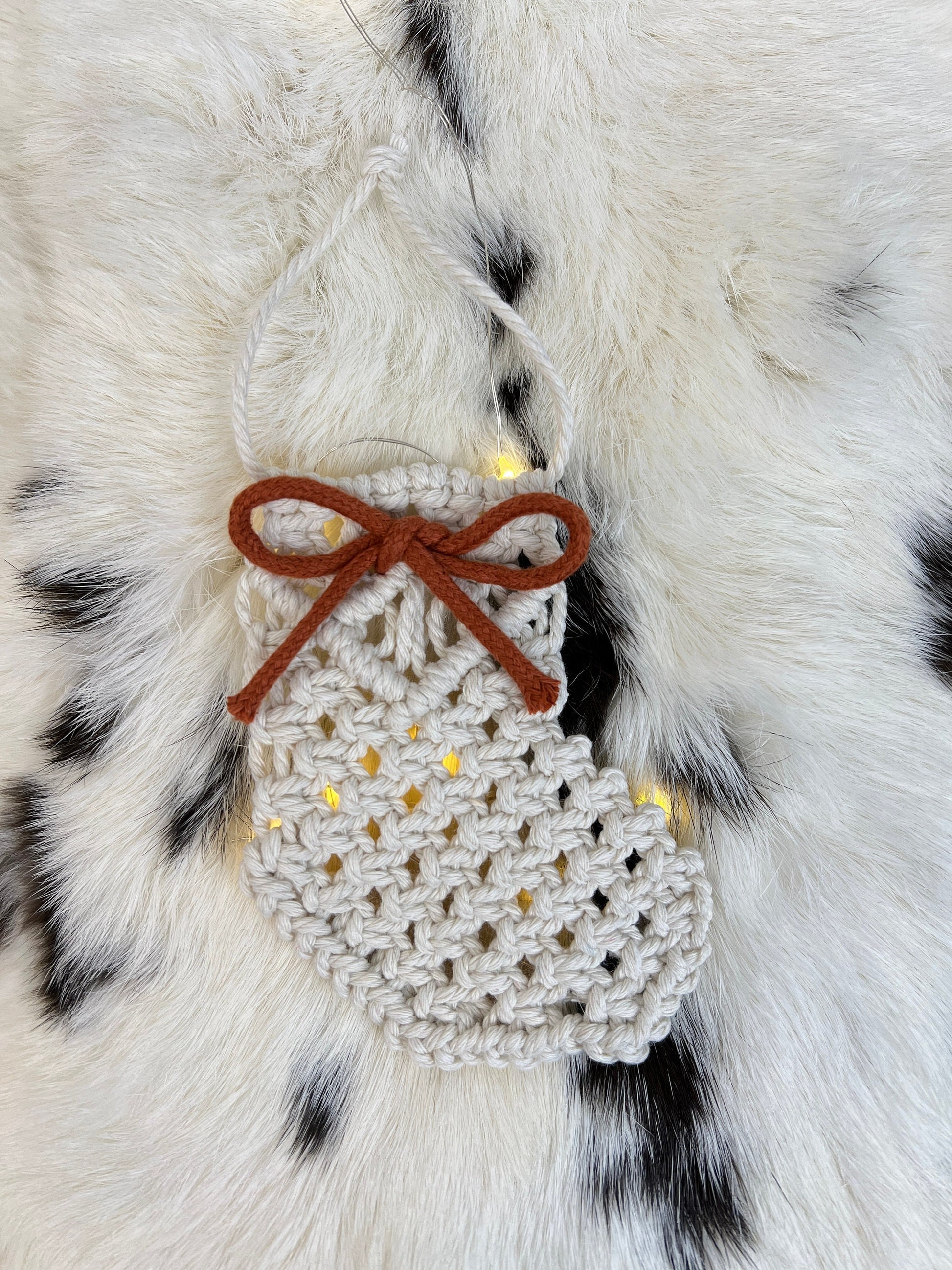 Decorative white macrame ornament with brown bow on a fur surface