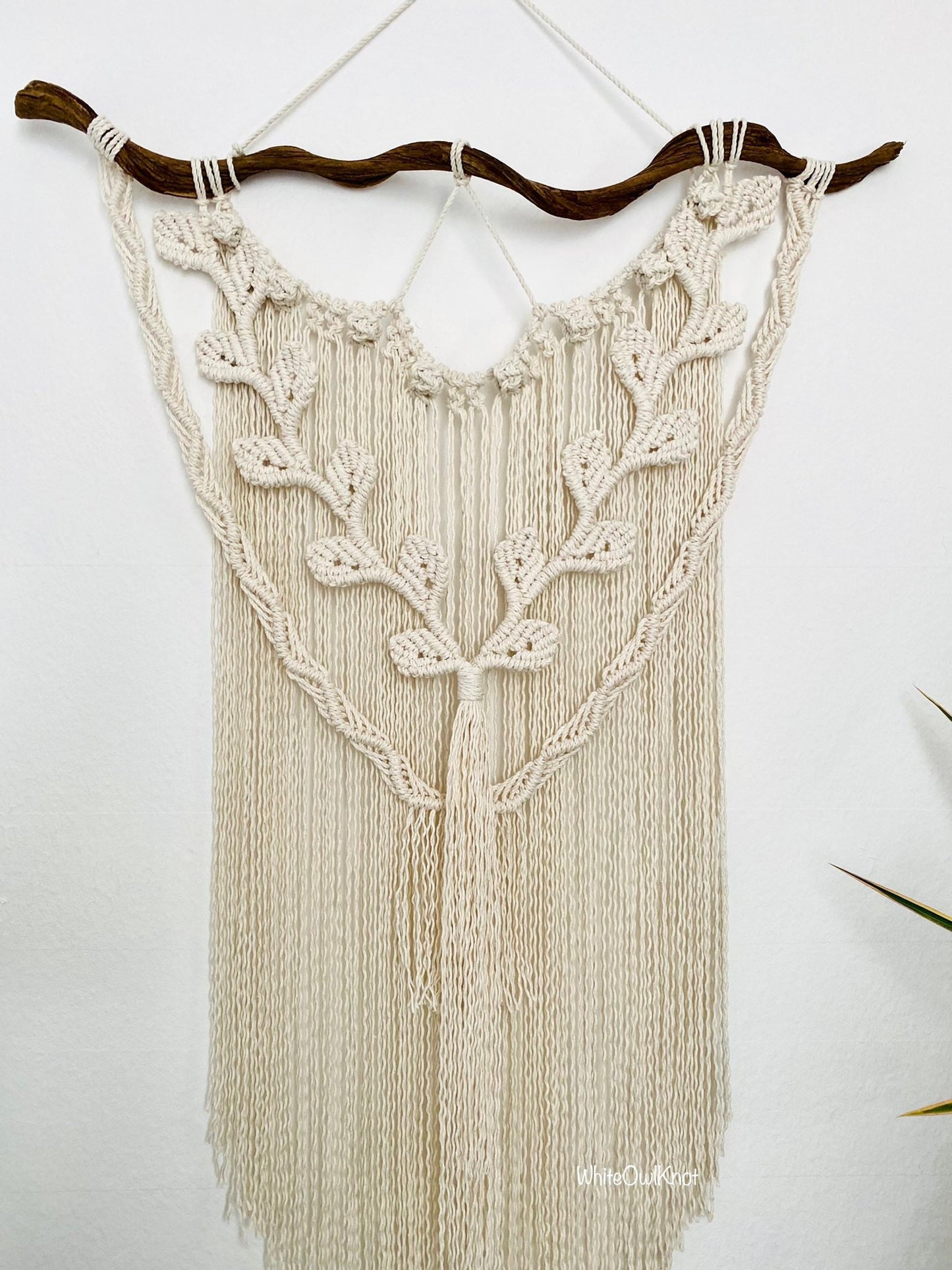 Macrame wall hanging with leaf patterns on a white wall