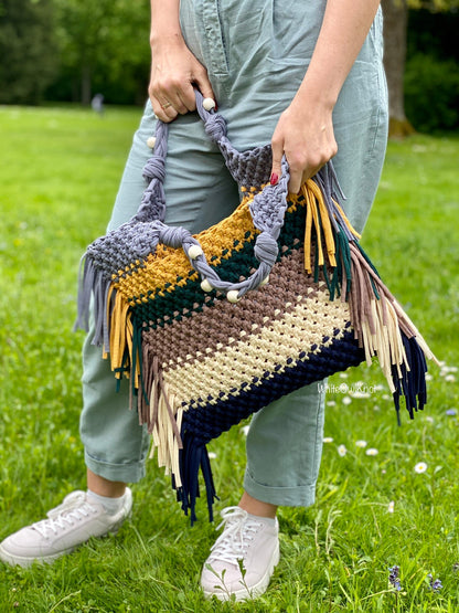 Person holding a colorful woven bag with fringes in a grassy outdoor setting