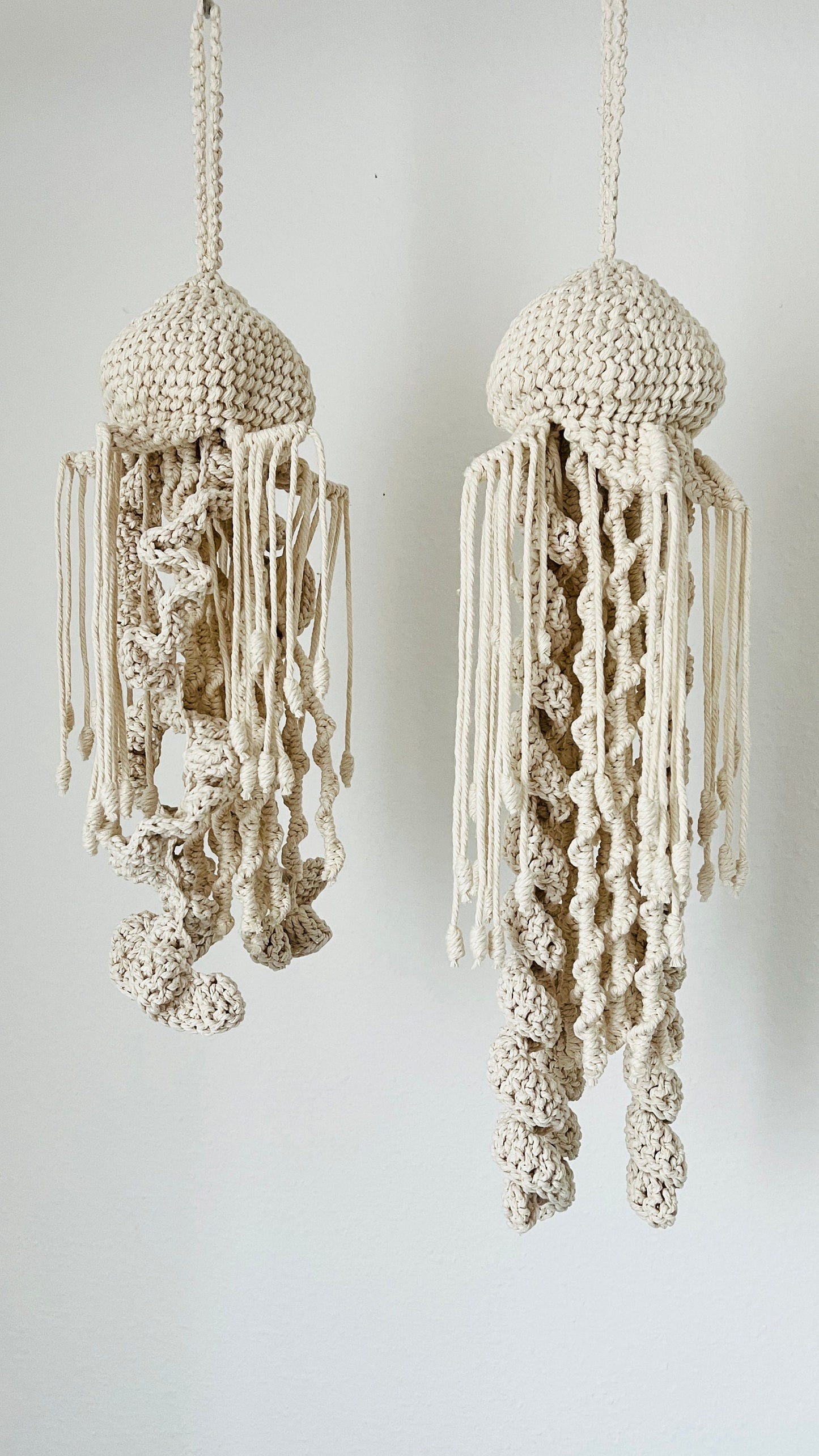 Two macrame knotted jellyfish decorations hanging against a white background