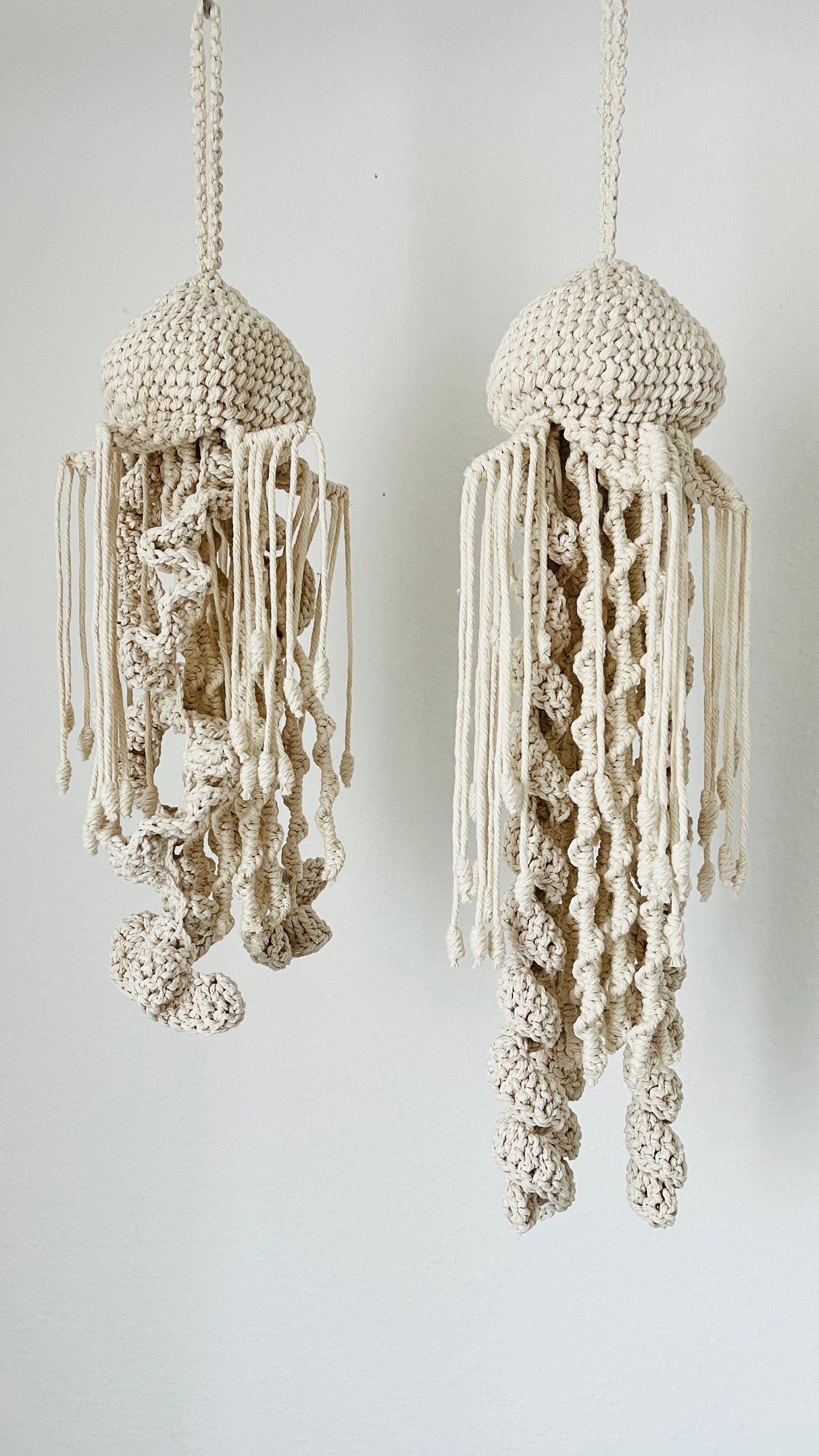 Two macrame knotted jellyfish decorations hanging against a white background