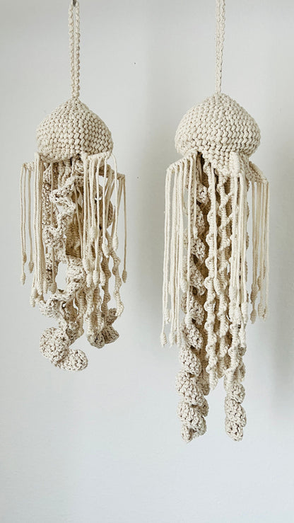 Two macrame knotted jellyfish decorations hanging against a white background