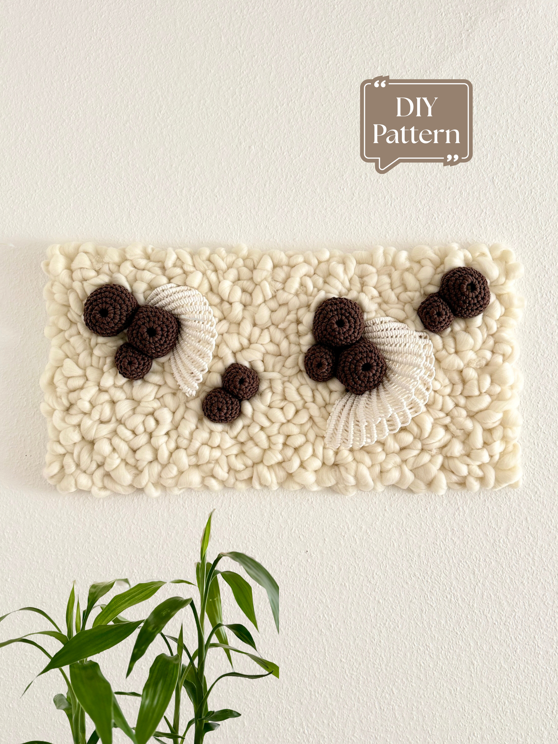 Fiber coral inspired wall art hanging on white wall above green plant, textured fiber art DIY pattern example
