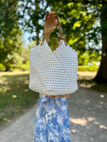 White woven handbag held by a person in a park setting