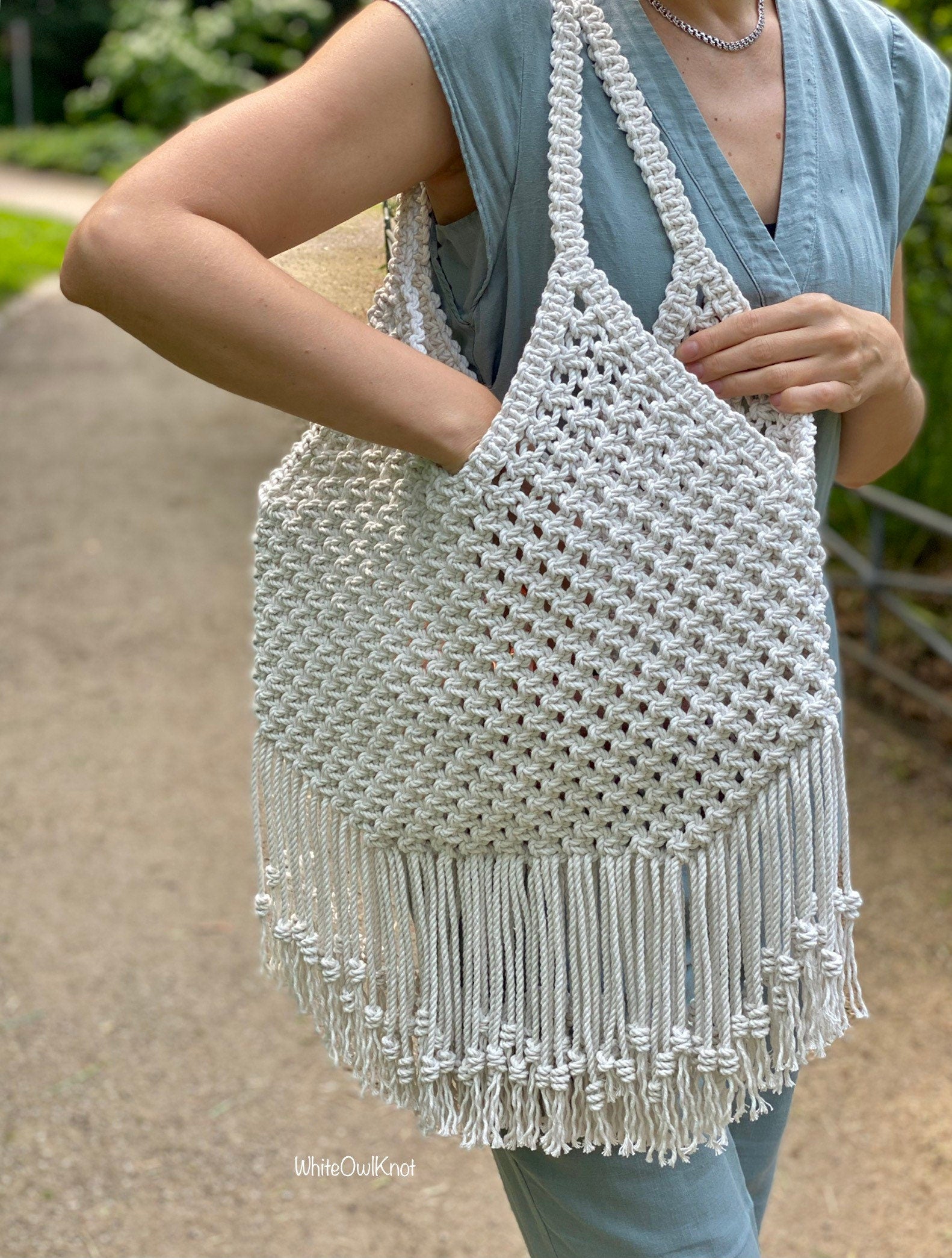 Person holding a woven bag with fringe outdoors