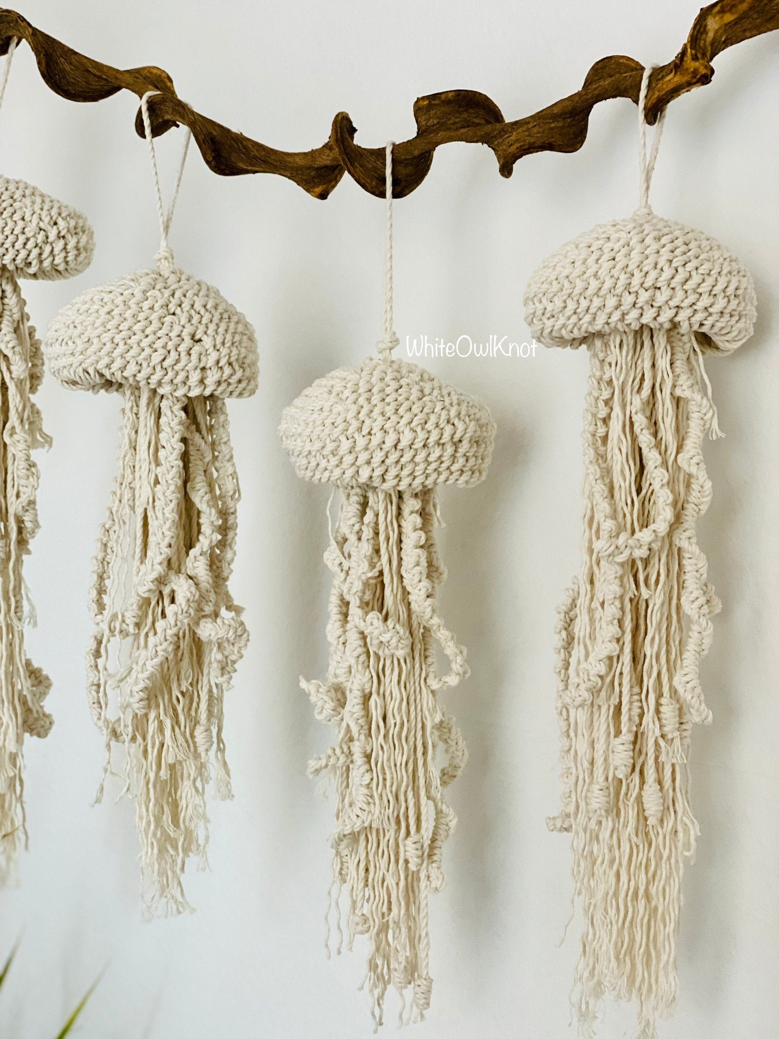 Macrame jellyfish decorations hanging from a branch against a white background