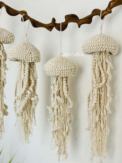 Macrame jellyfish decorations hanging from a branch against a white background