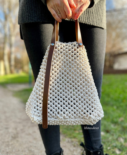 Person holding a woven macrame handbag with brown straps outdoors.