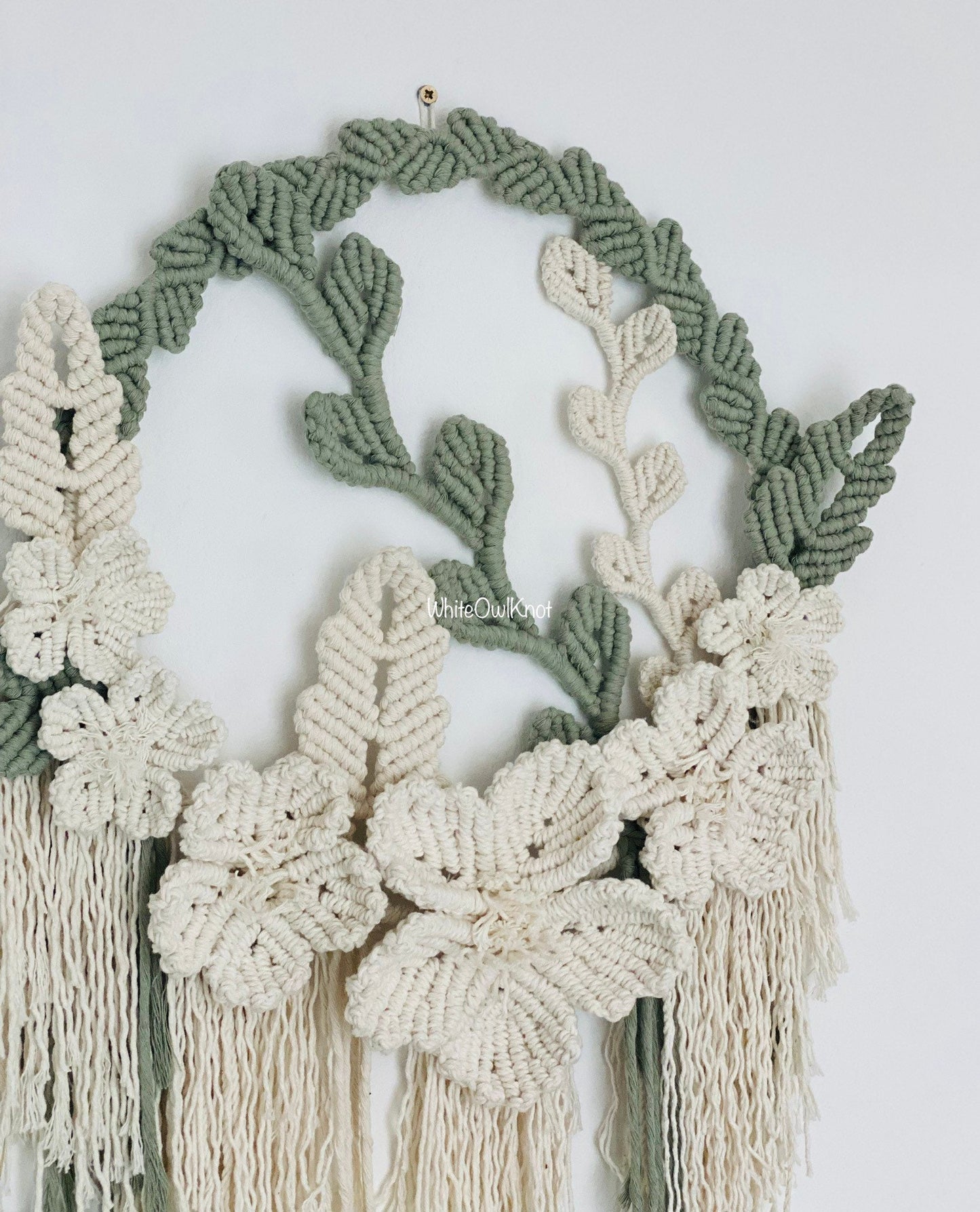 Macrame wall hanging with green and white leaves on a plain background