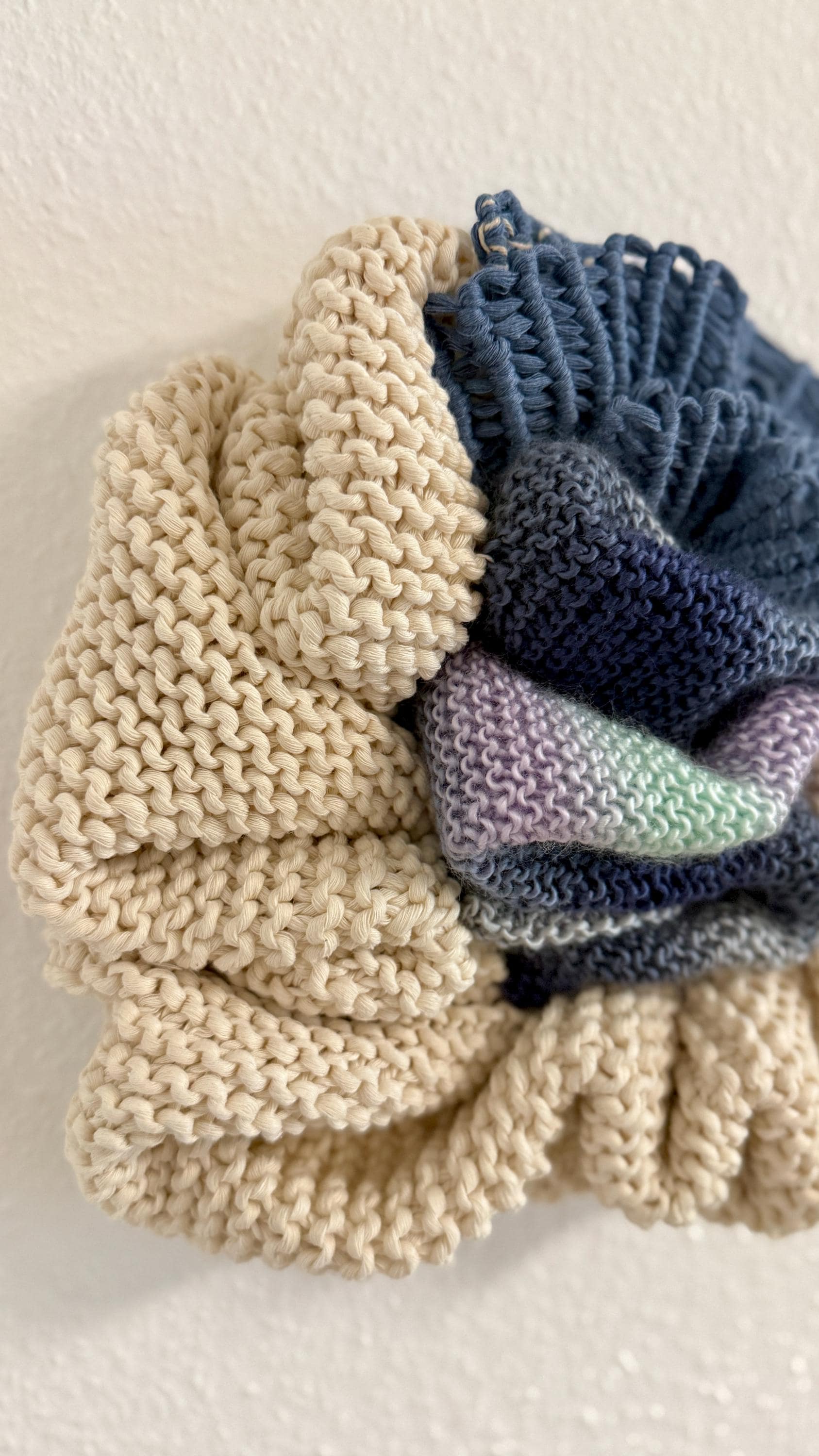 Knitted fiber art with details, one beige and one with gradient colors, on a light background.